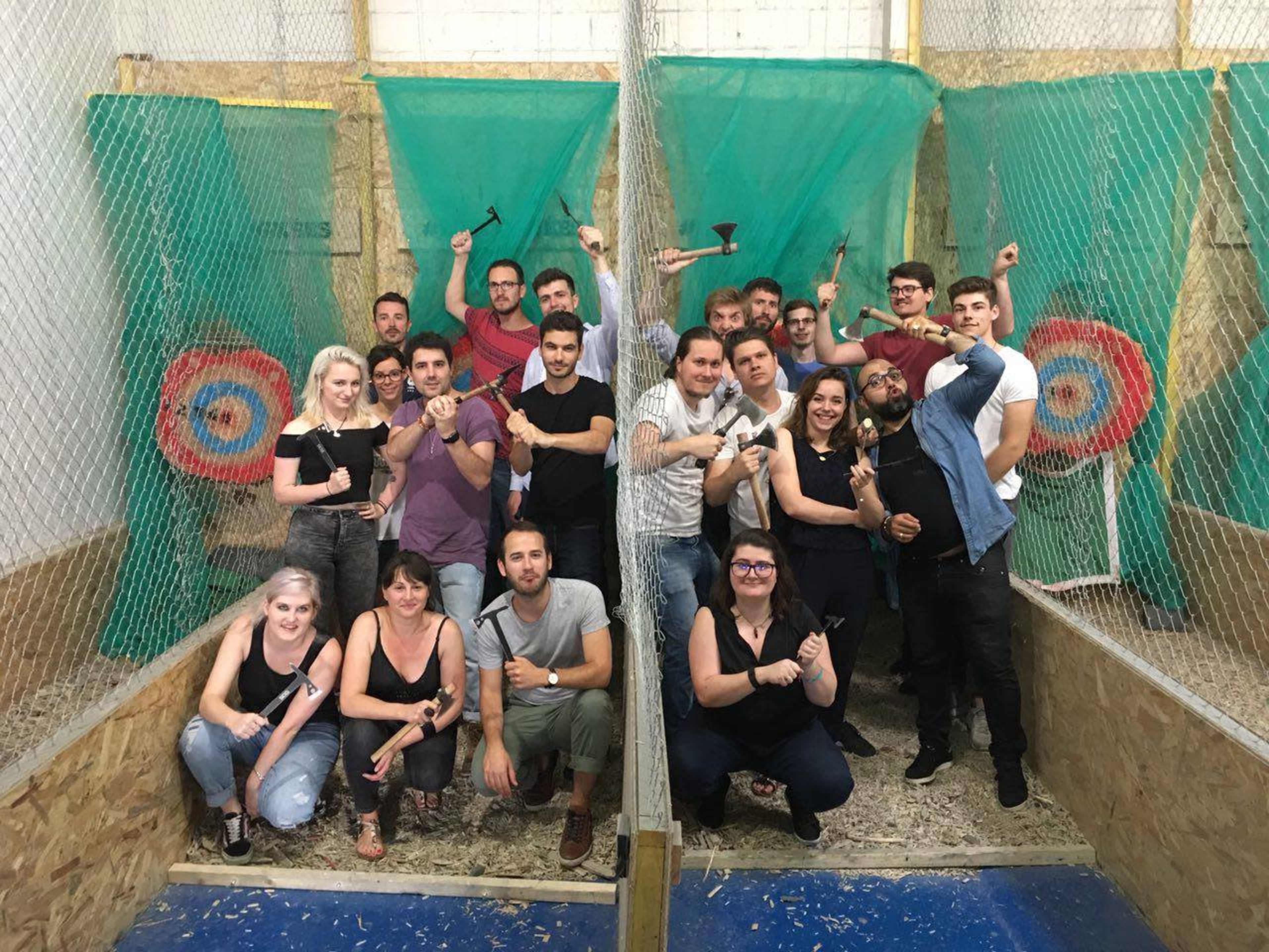 A large group of people poses with axes in an indoor axe-throwing venue, standing in front of target boards.