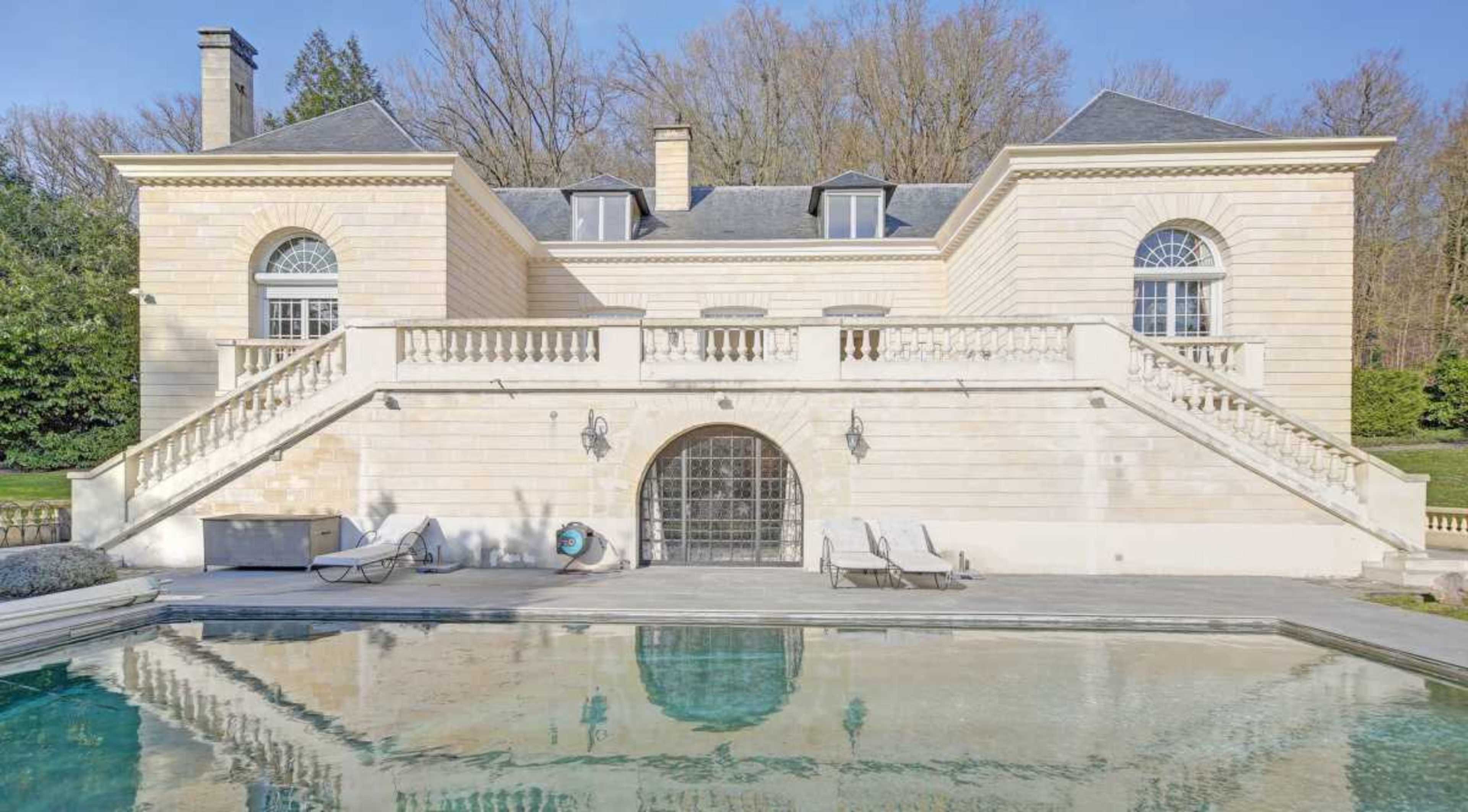 The image shows a large stone mansion with a tiered entrance, a balcony, and a reflecting pool in front.
