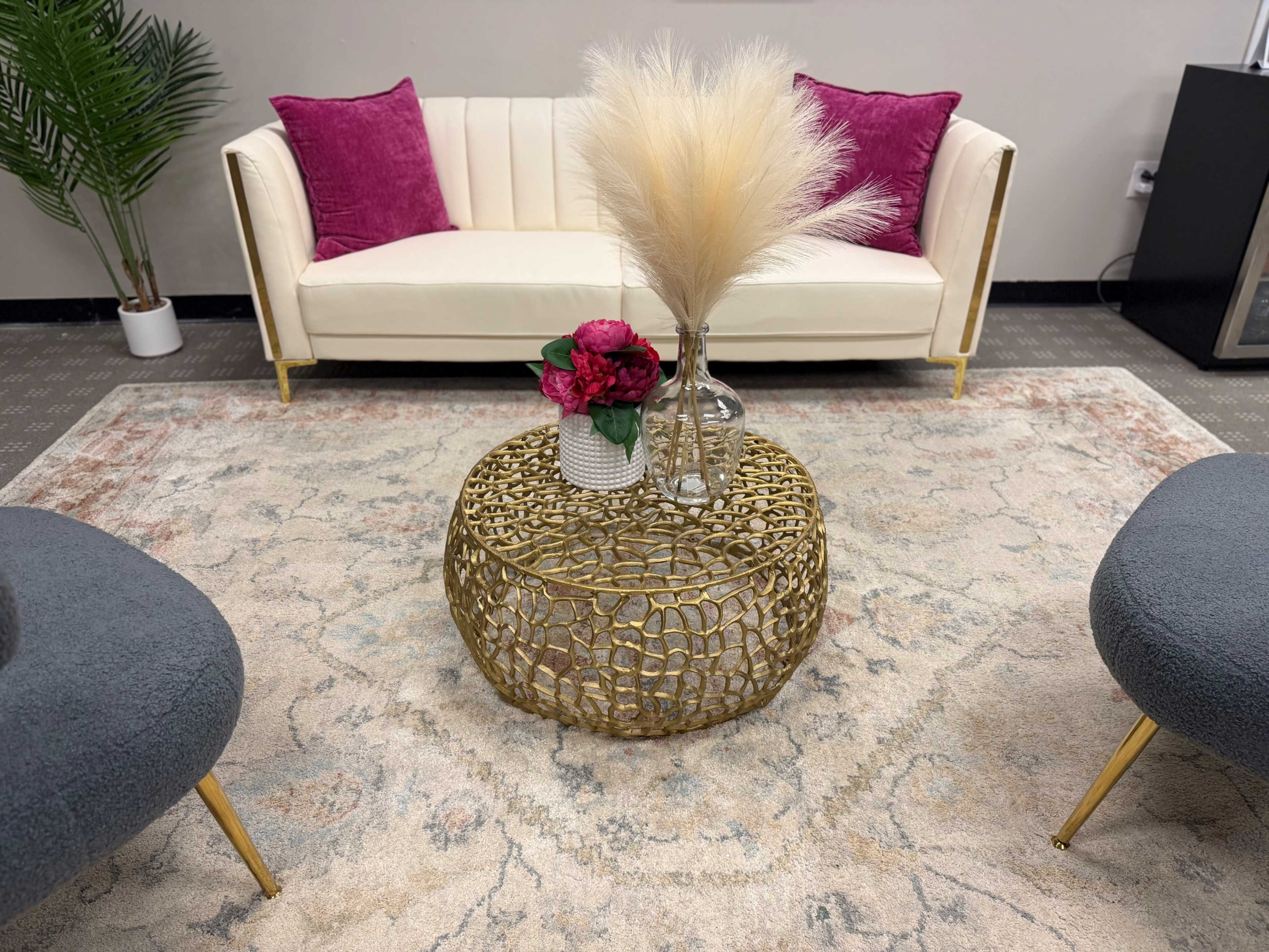 A cream-colored sofa with pink cushions sits in a stylized living area, complemented by a decorative gold coffee table featuring flowers in a vase.