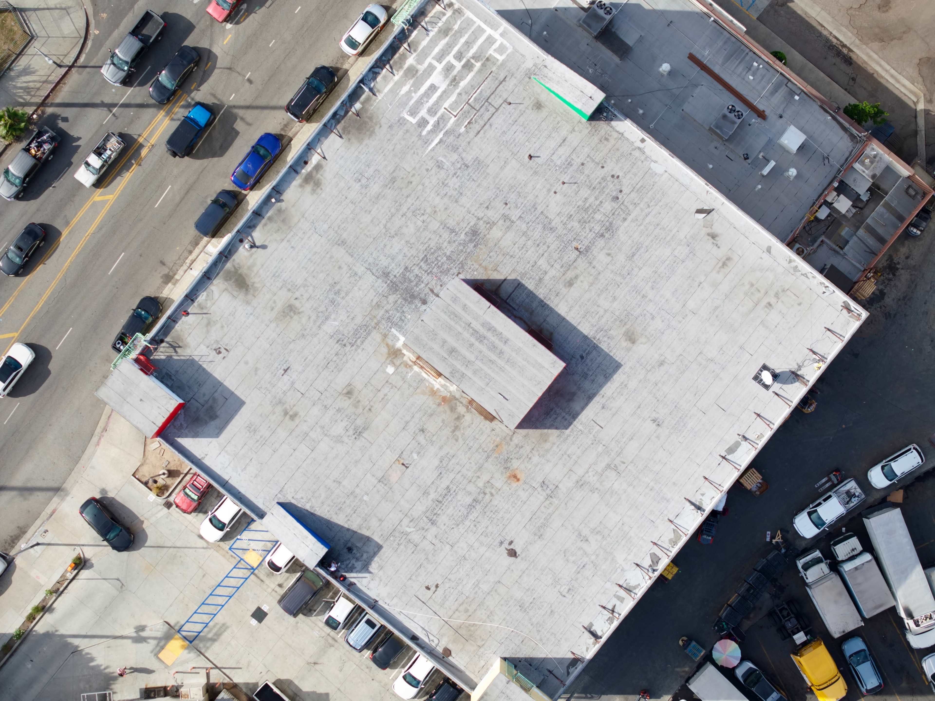 An overhead view shows a flat-roofed building with a central structure, surrounded by parked cars on nearby streets.