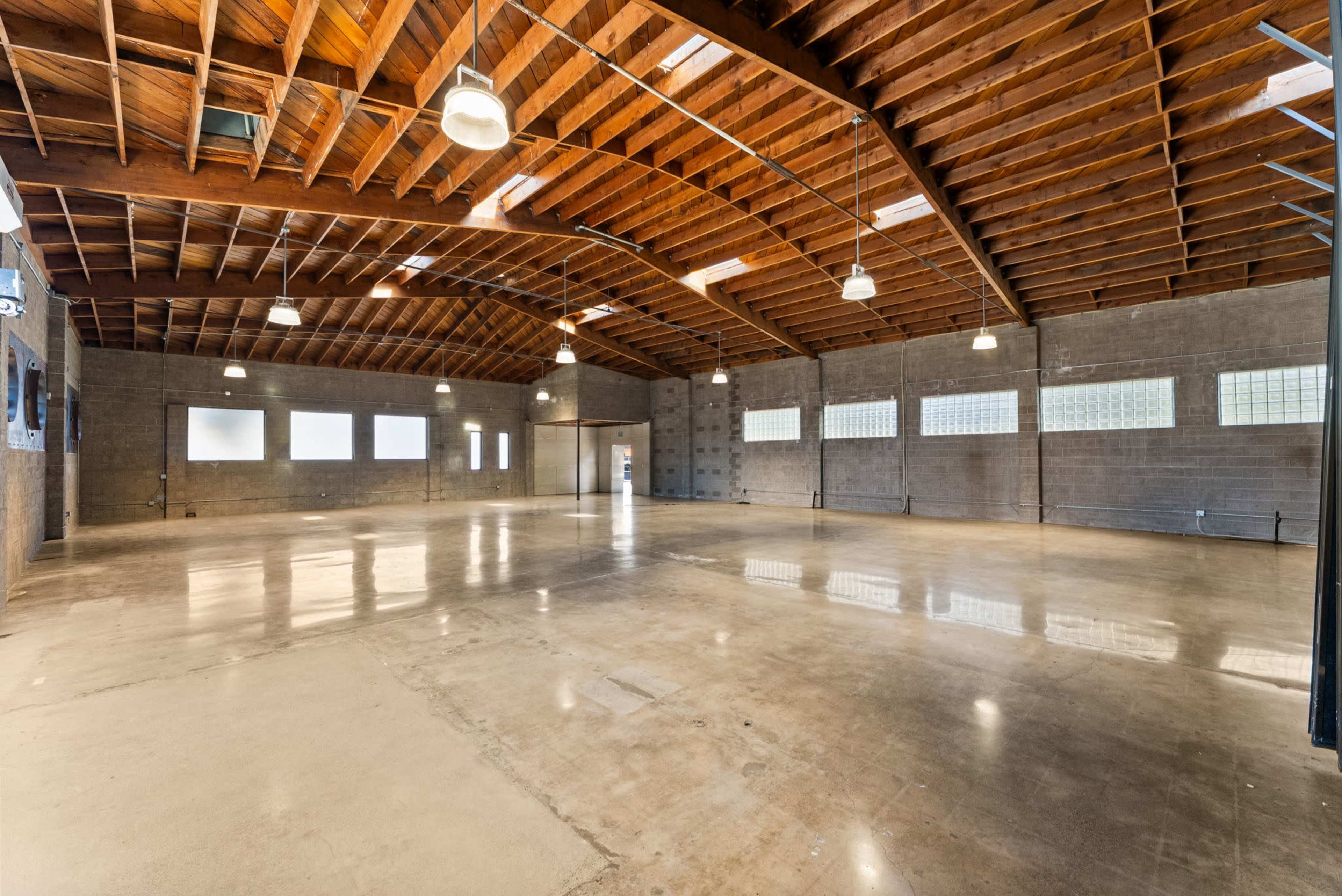 The image shows a spacious interior room with polished concrete floors, high wooden ceilings, and several overhead lights.
