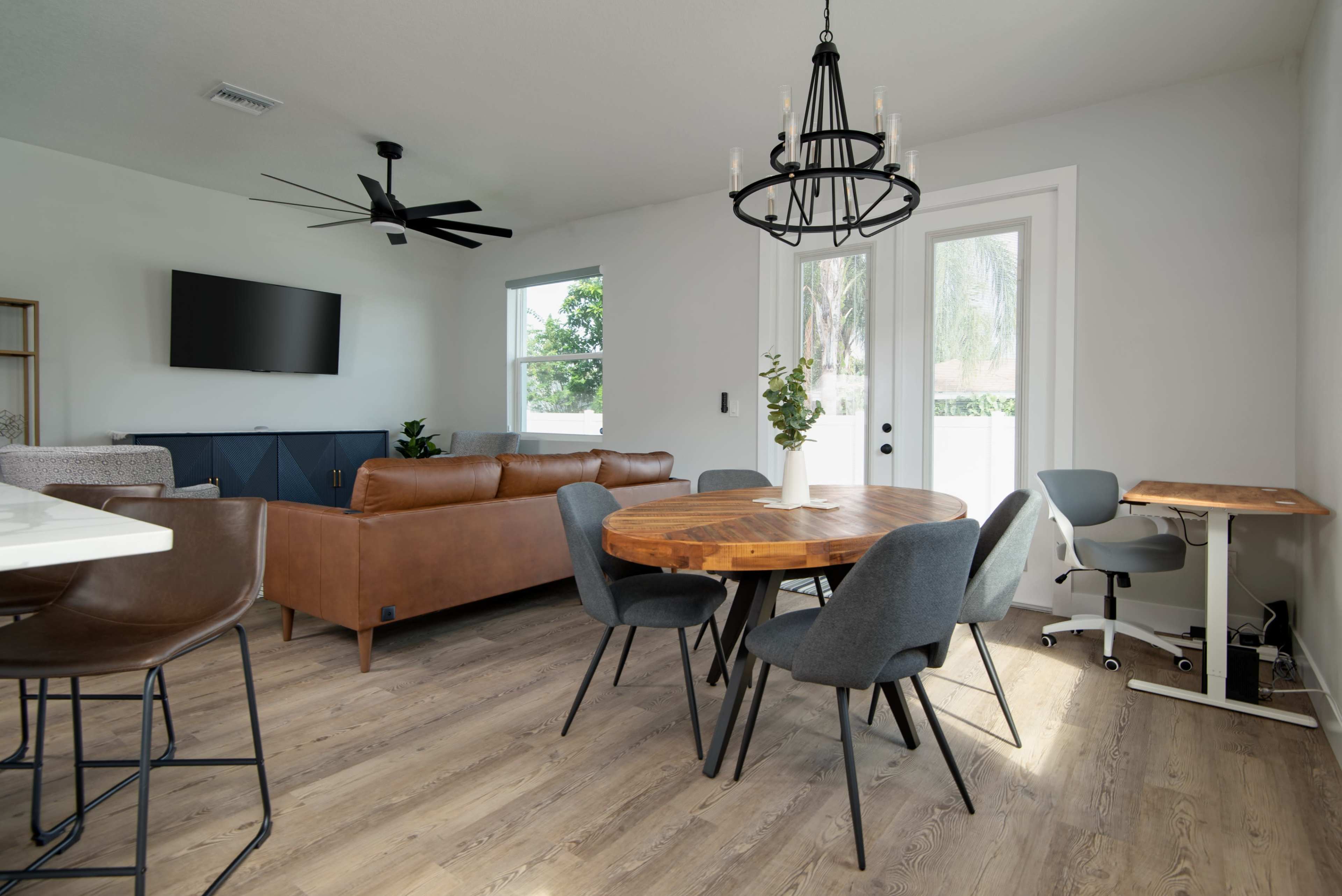 A modern living and dining area featuring a round wooden table surrounded by gray chairs, a brown leather sofa, and a large wall-mounted television.