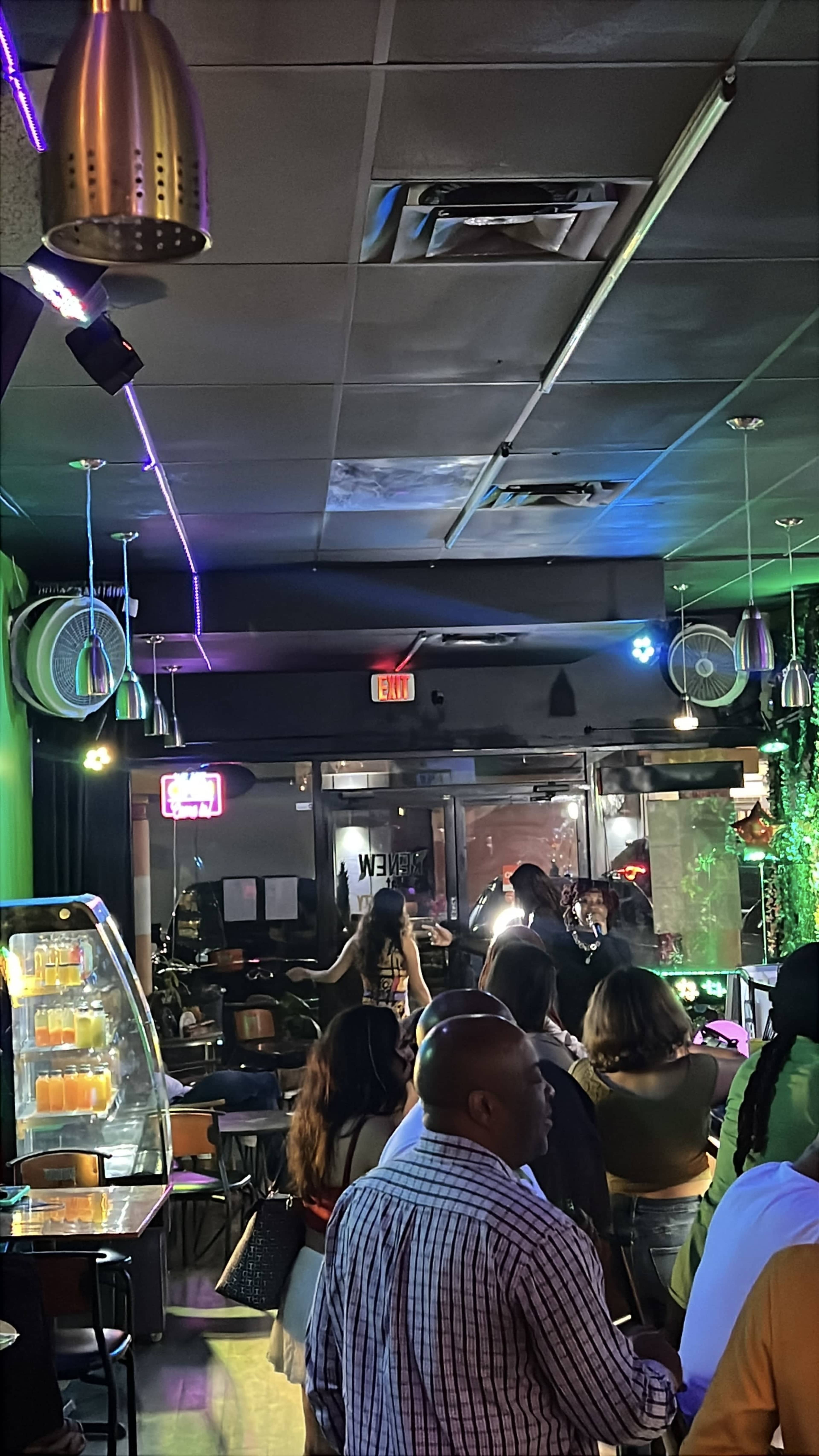 The image shows a crowded indoor bar or lounge with neon lights and patrons waiting in line.