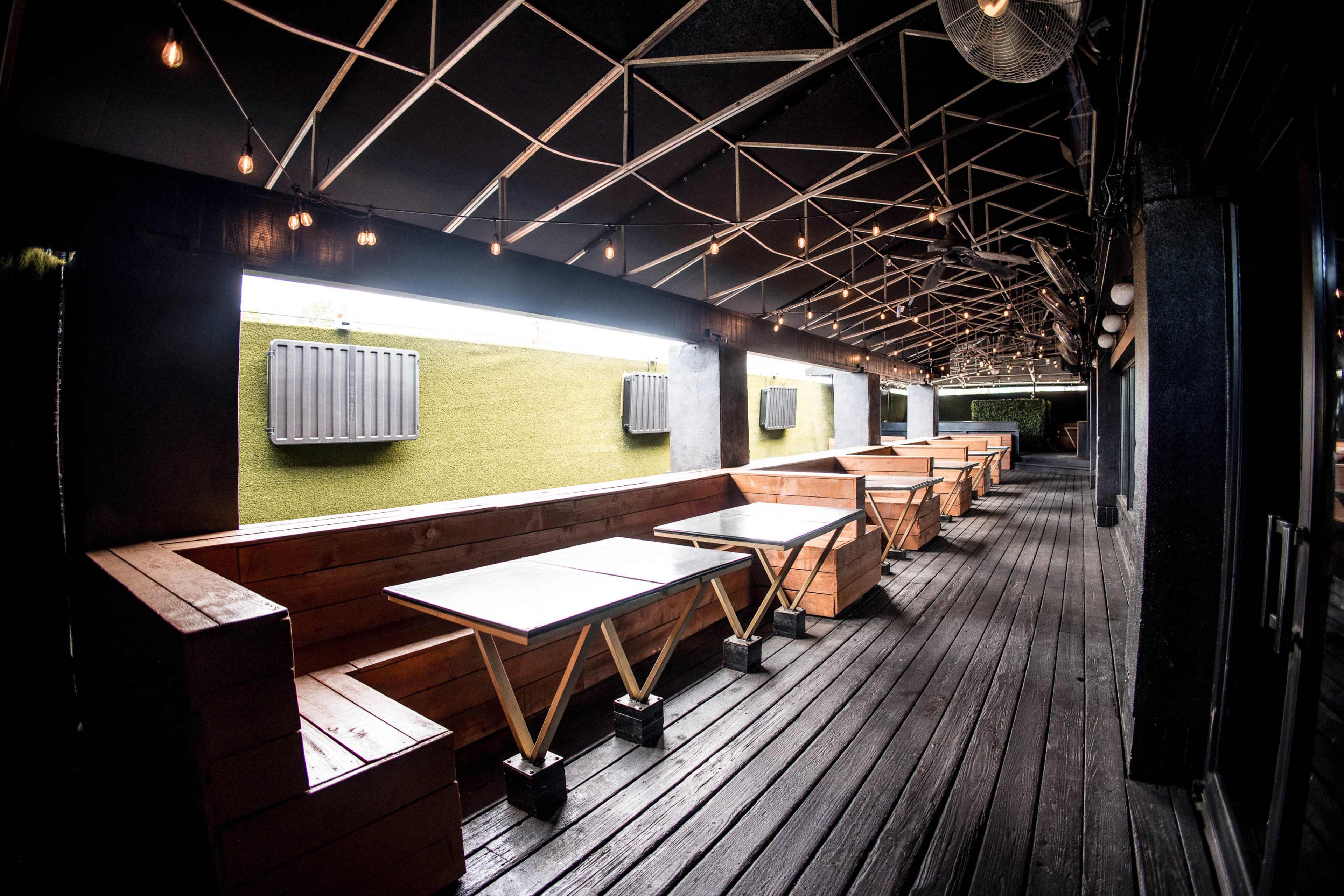 A long outdoor seating area features wooden tables and benches under a decorative ceiling with hanging lights.