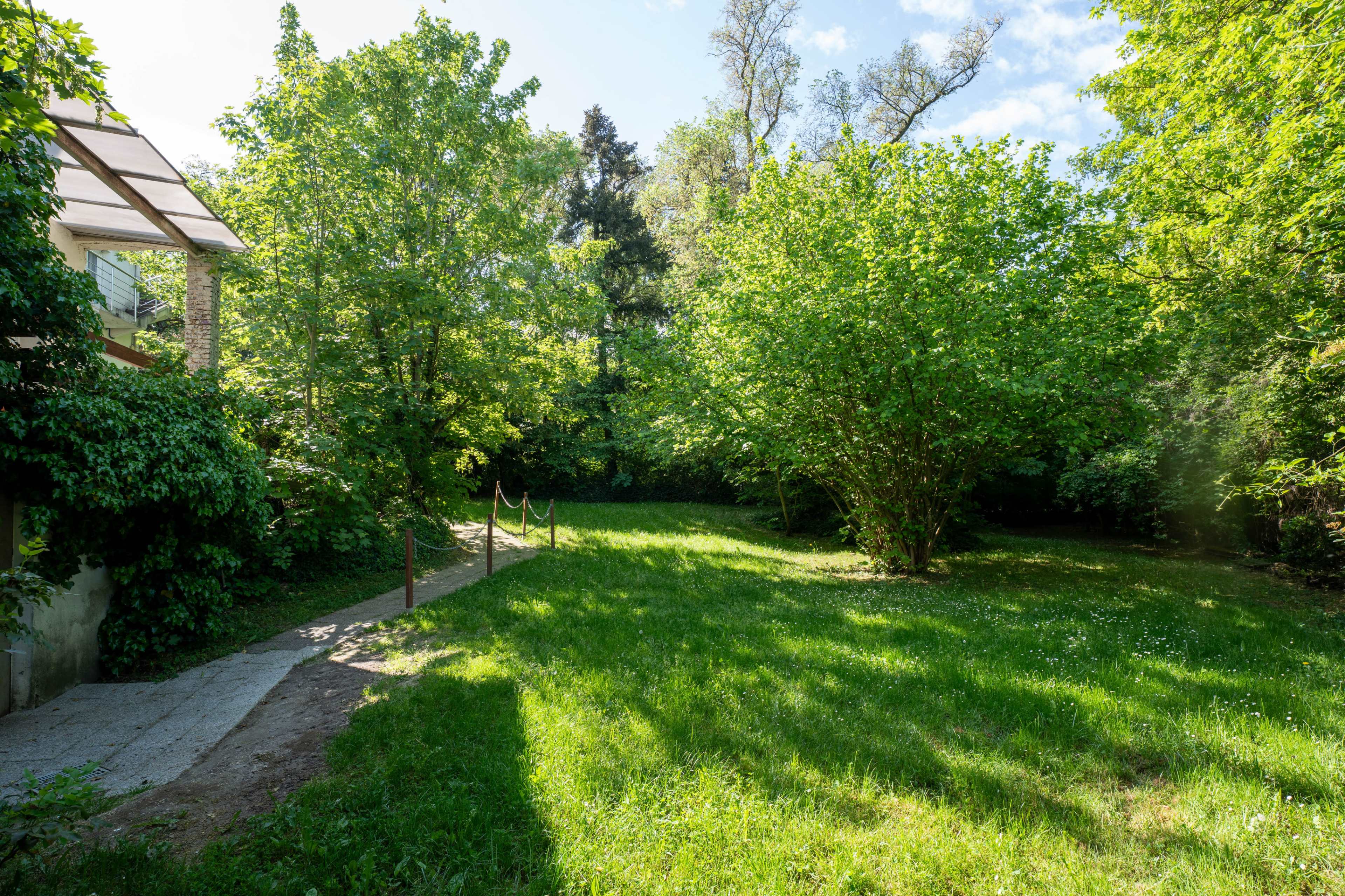 A grassy area surrounded by trees and a pathway leading to a building is visible in the image.