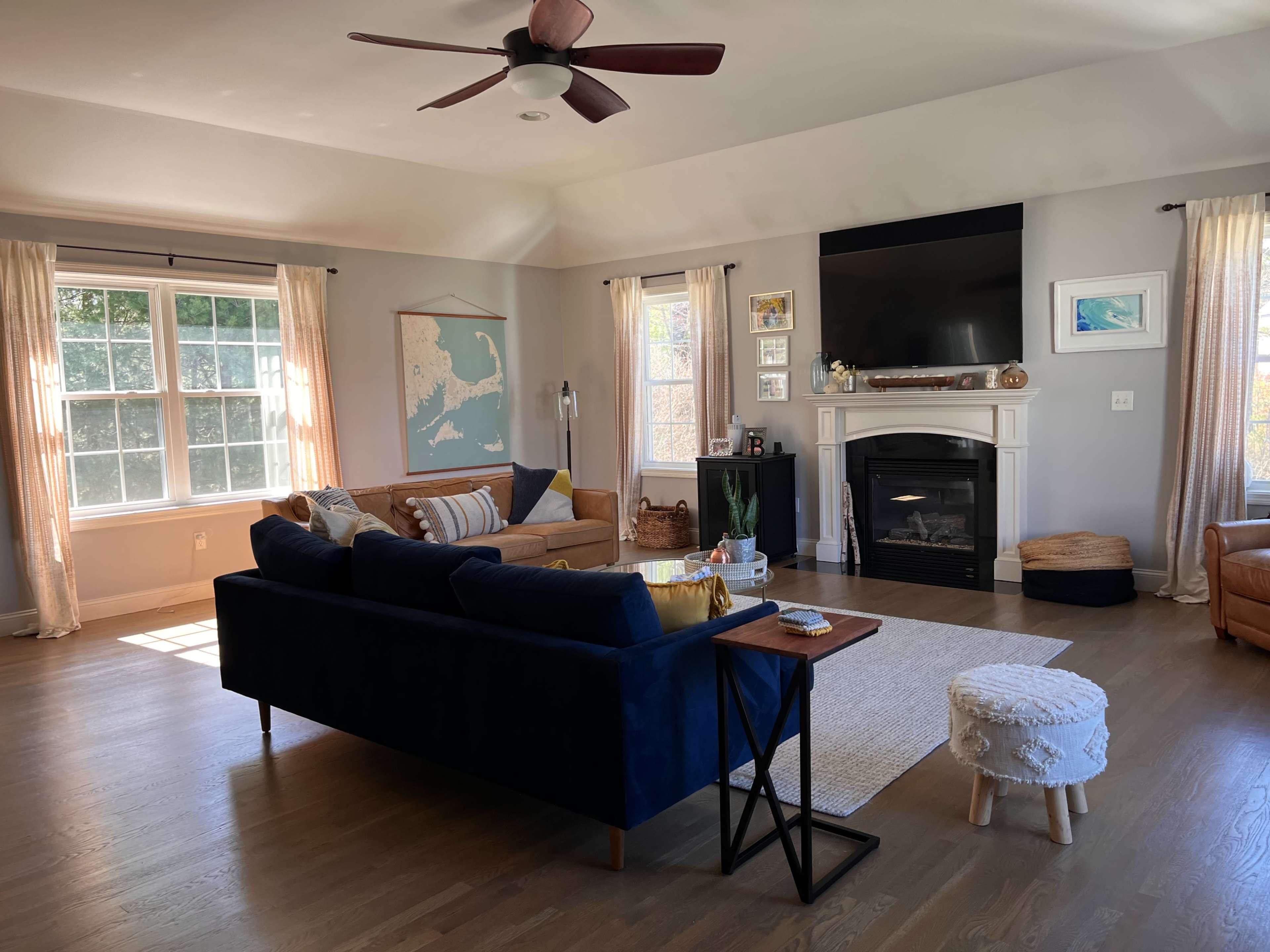 The living room features a navy blue couch, a brown leather armchair, a large window with sheer curtains, and a fireplace with a television above it.