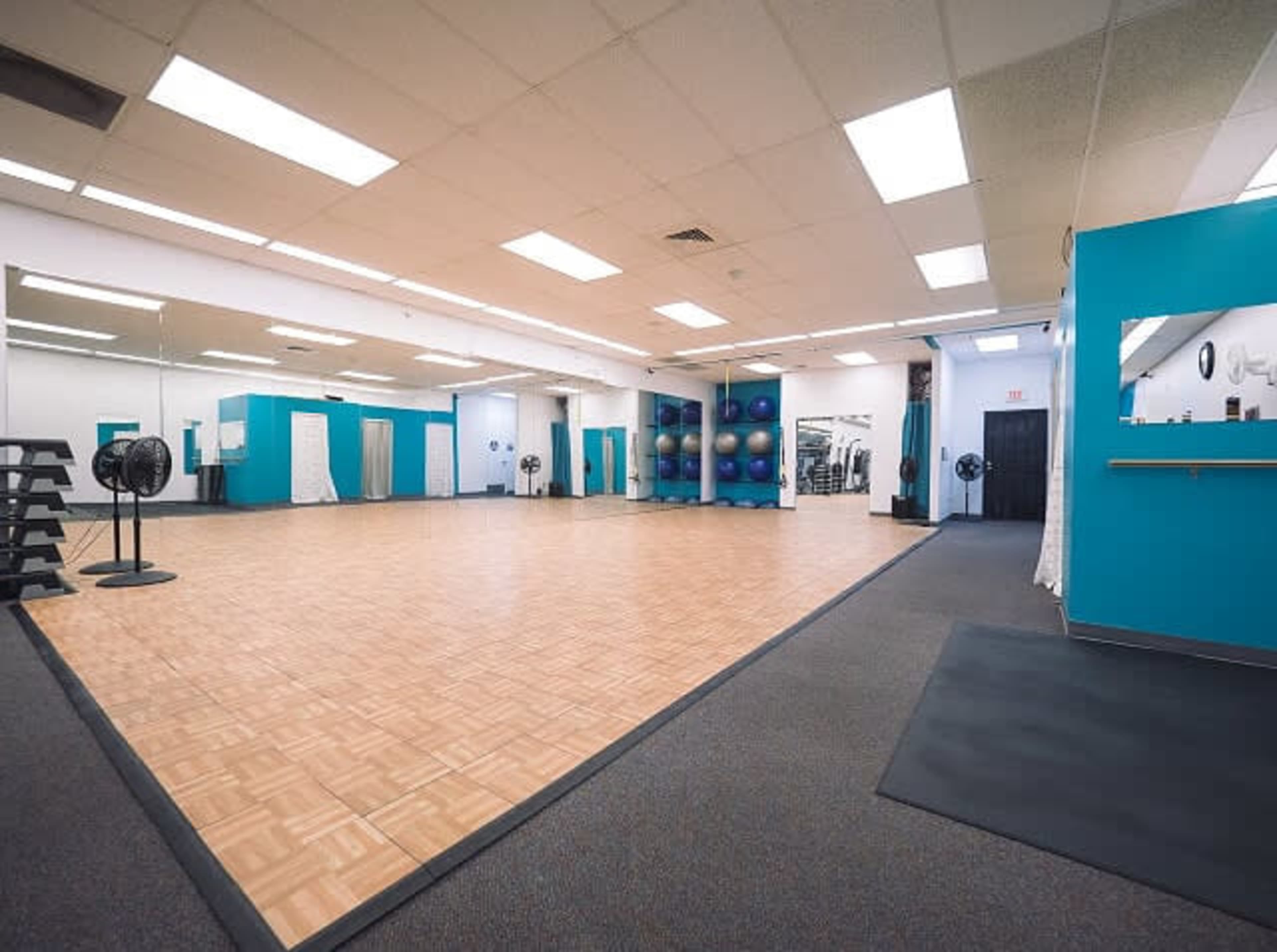 A spacious exercise studio with wooden flooring, mirrors on one wall, and fitness equipment along the side.