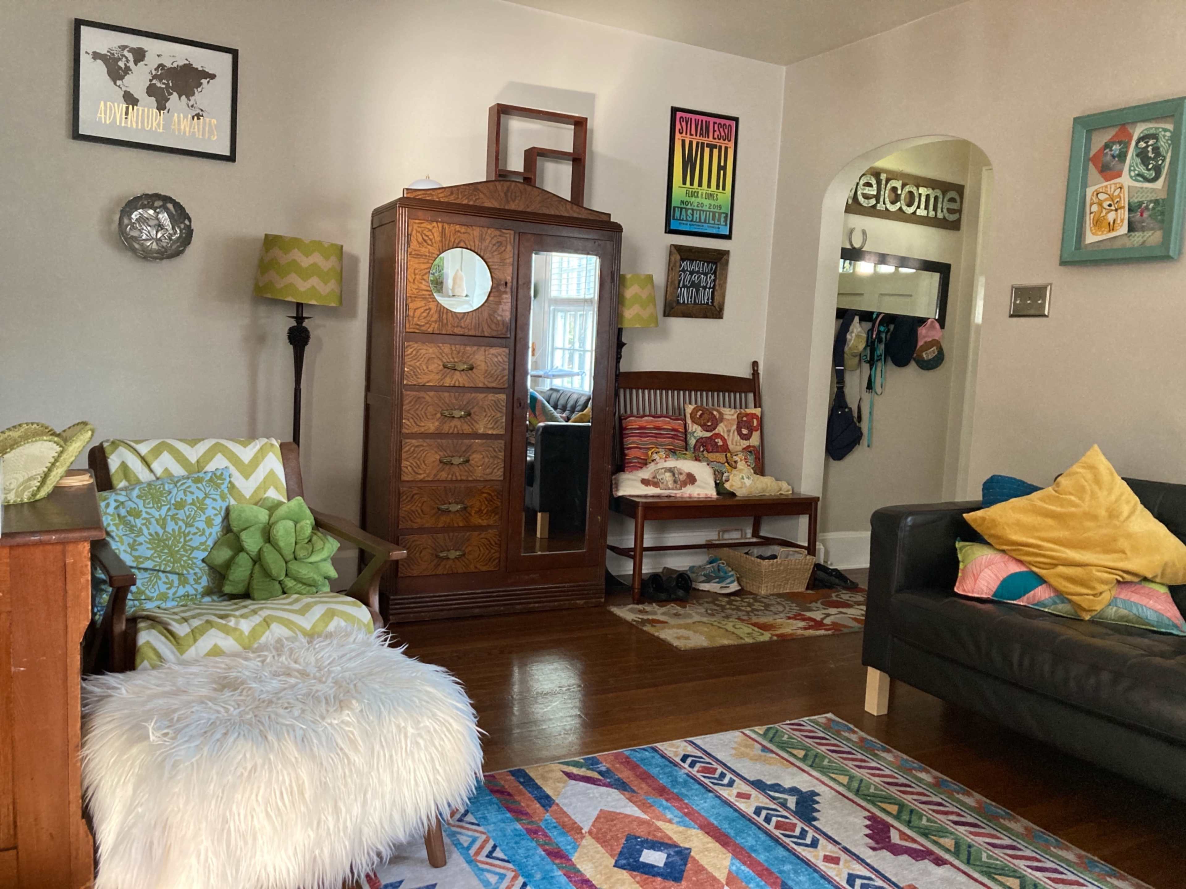 A cozy living room featuring a mixture of furniture including a patterned rug, a shelf with wall art, and a decorative wooden dresser.
