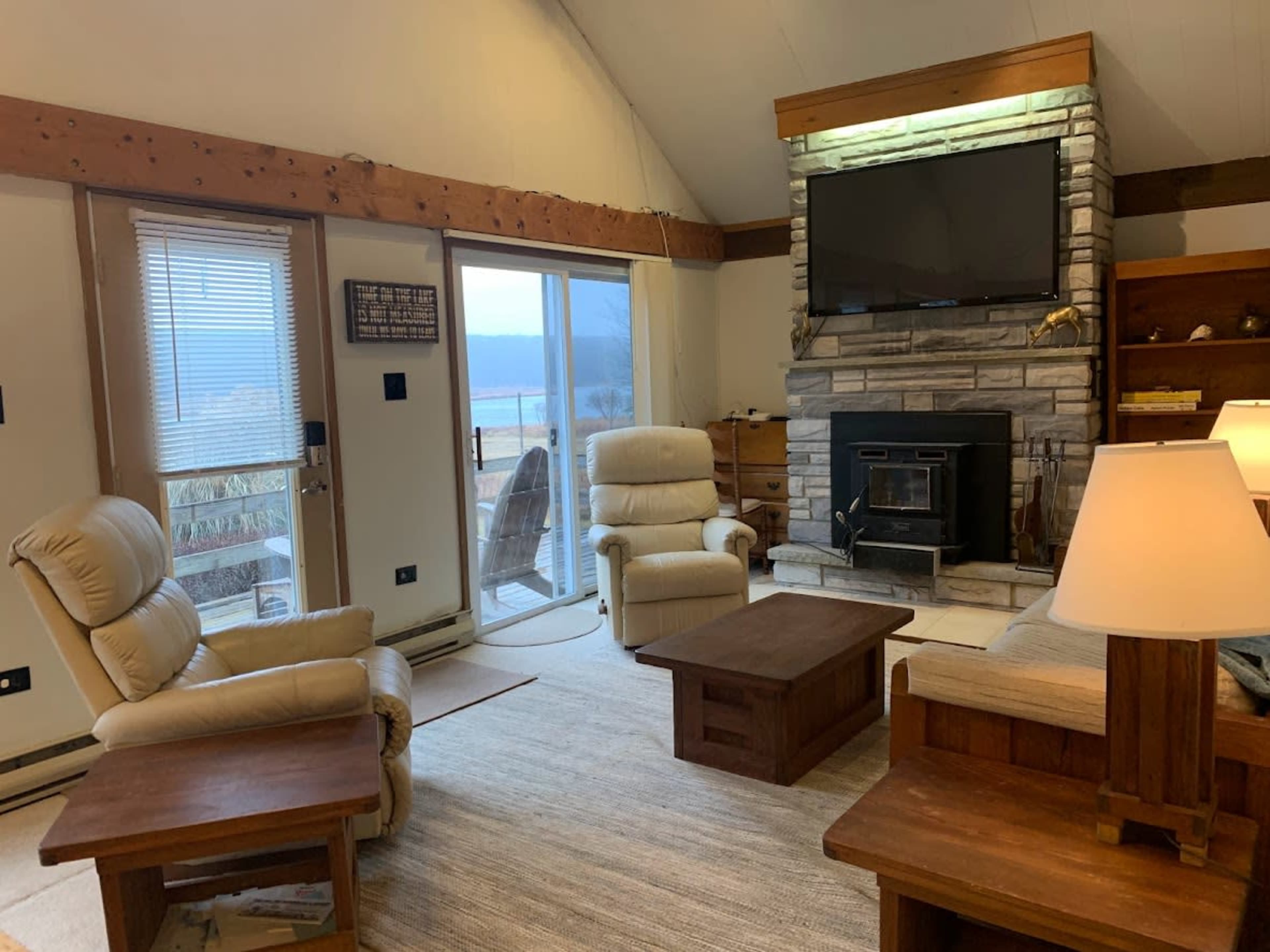 The living room features two reclining chairs, a fireplace with a television above it, and large windows that open to a scenic view.
