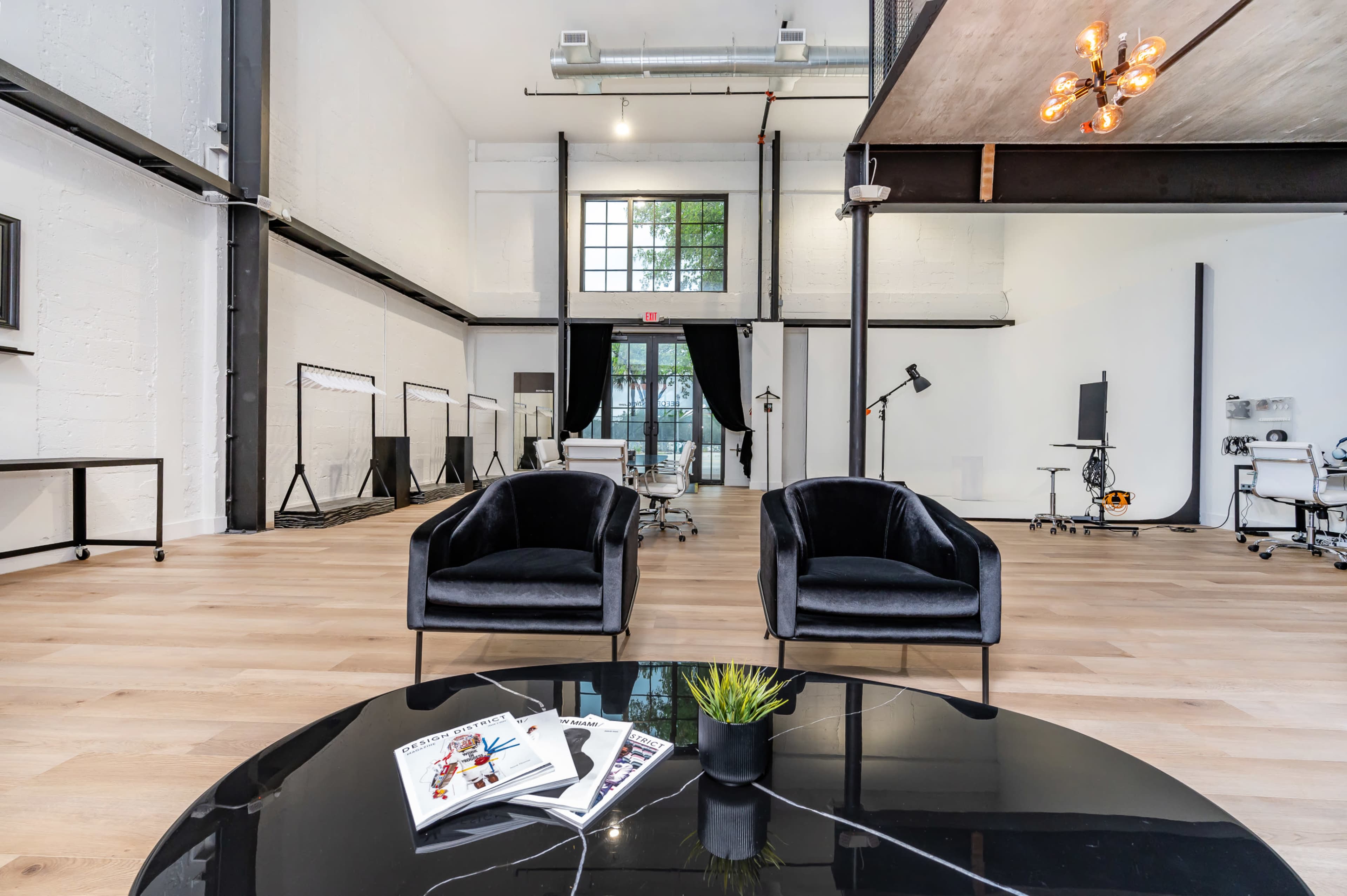 A modern, open space with two black chairs facing a coffee table, surrounded by a bright, minimalist interior featuring large windows and industrial elements.