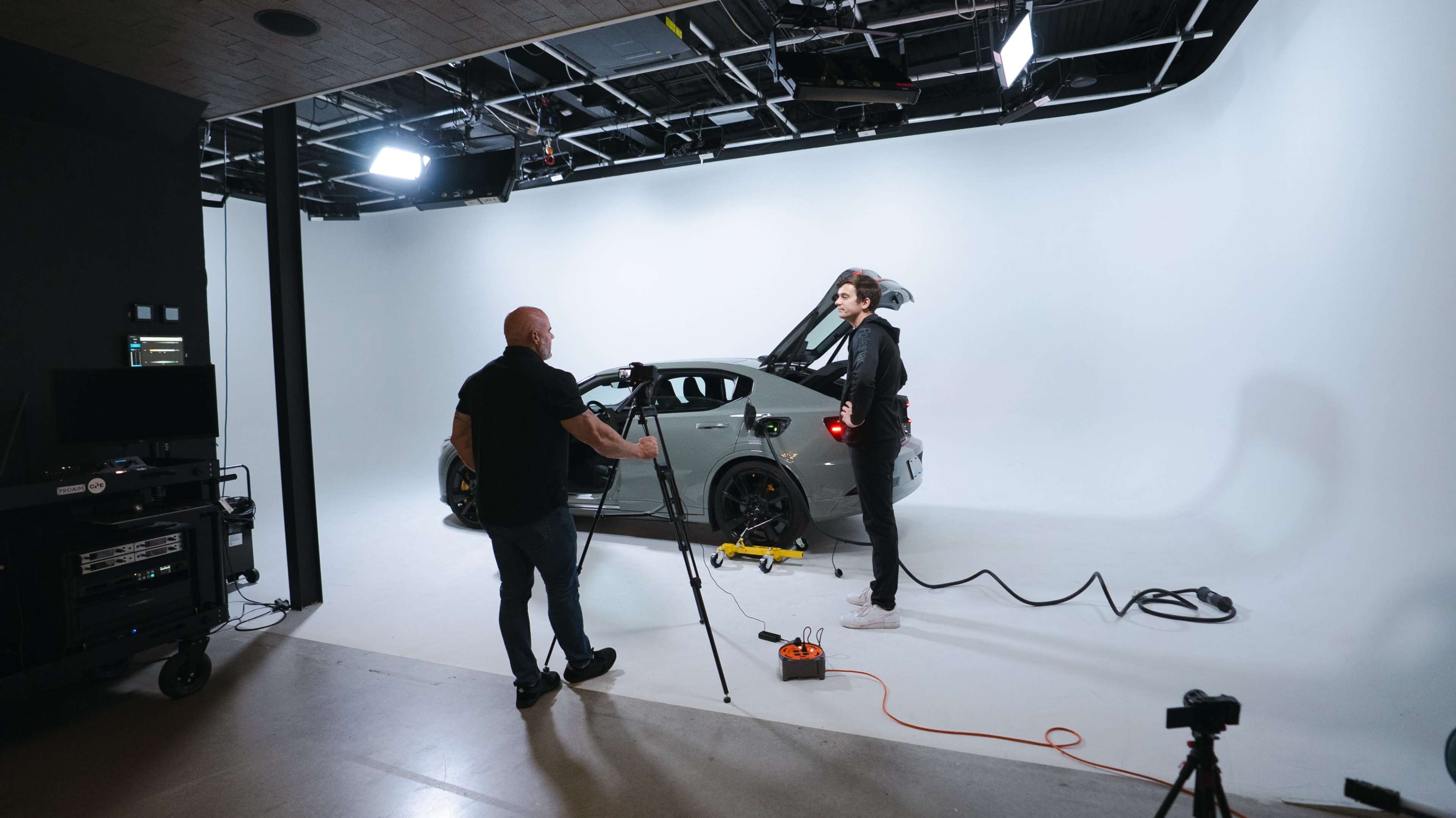 A photographer is setting up equipment to take pictures of a sports car in a studio with a plain white background.