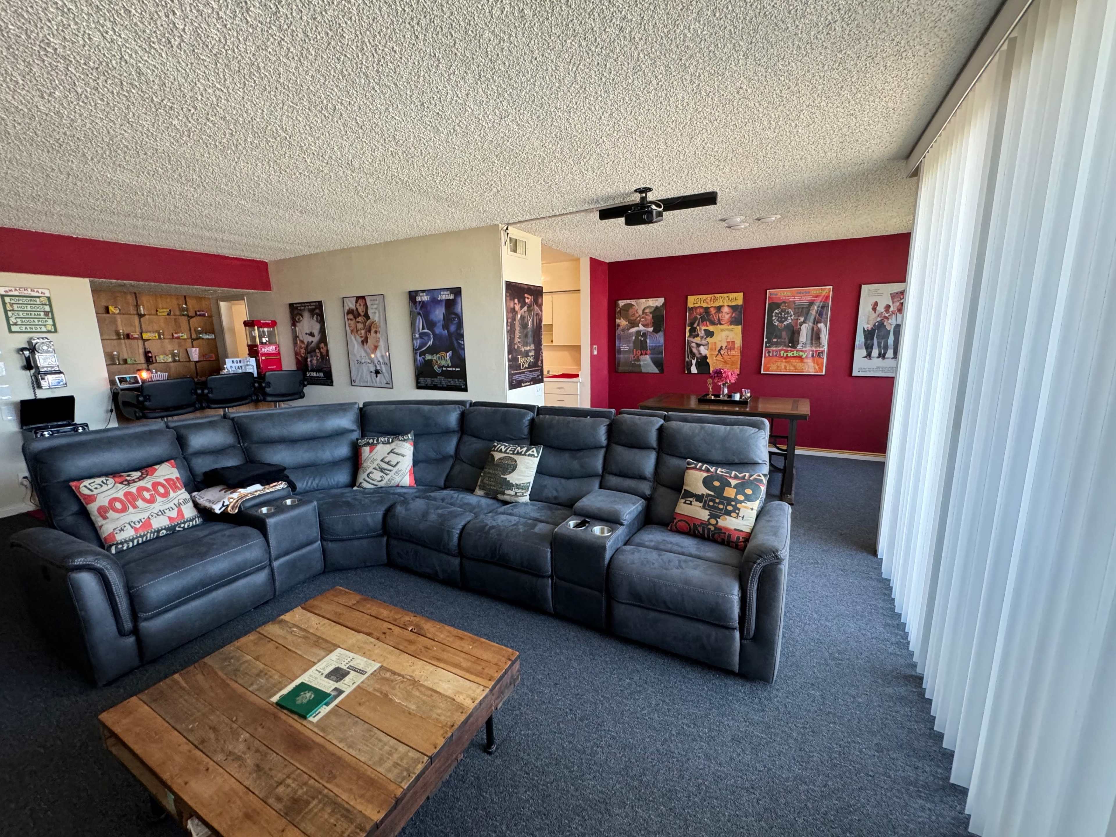 A modern living room features a large dark sectional sofa, a wooden coffee table, and walls adorned with movie posters.