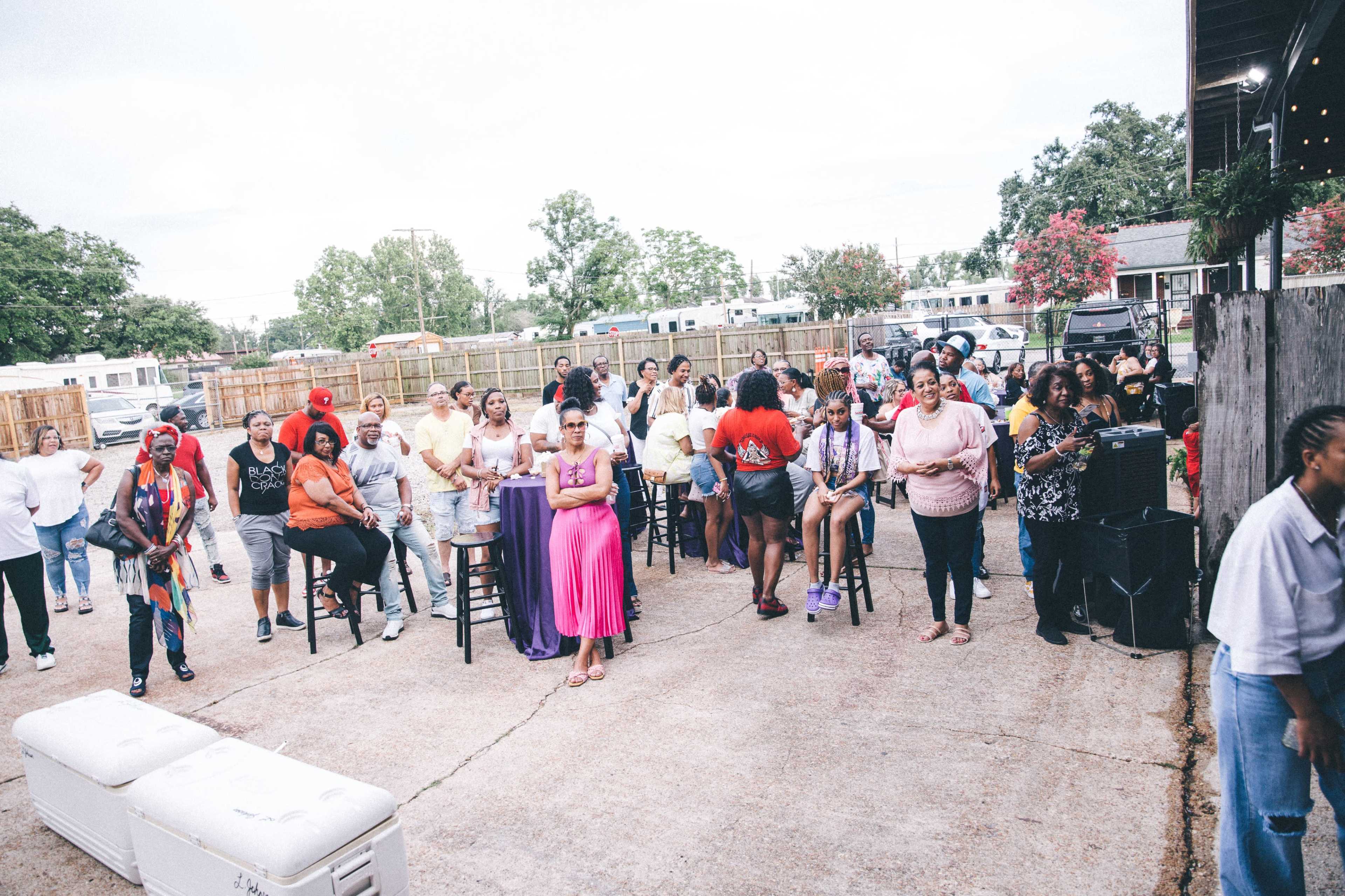 A crowd of people gathers in an outdoor space, with some standing near tall tables and others seated or mingling.
