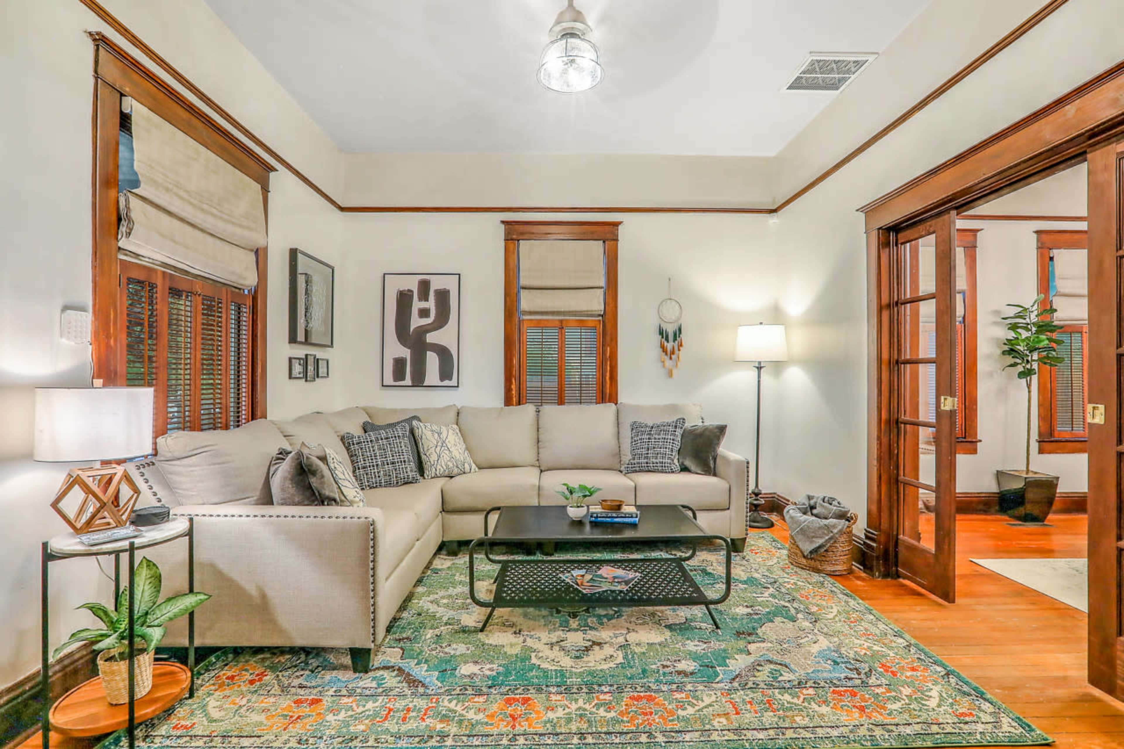 A cozy living room features a sectional sofa, a coffee table, and decorative plants, with warm wooden accents and soft lighting.