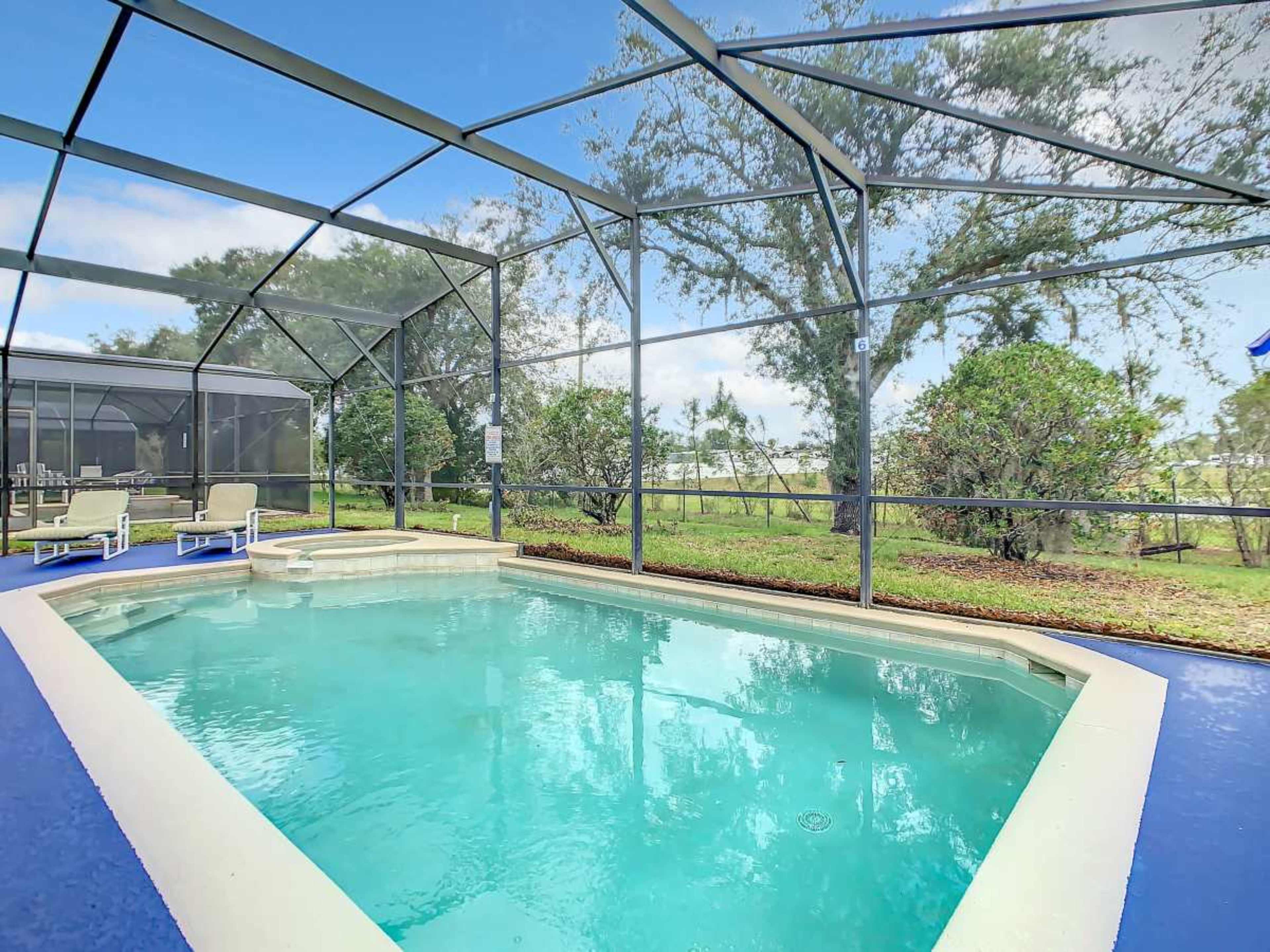 The image shows a screened-in swimming pool surrounded by green trees and lawn.
