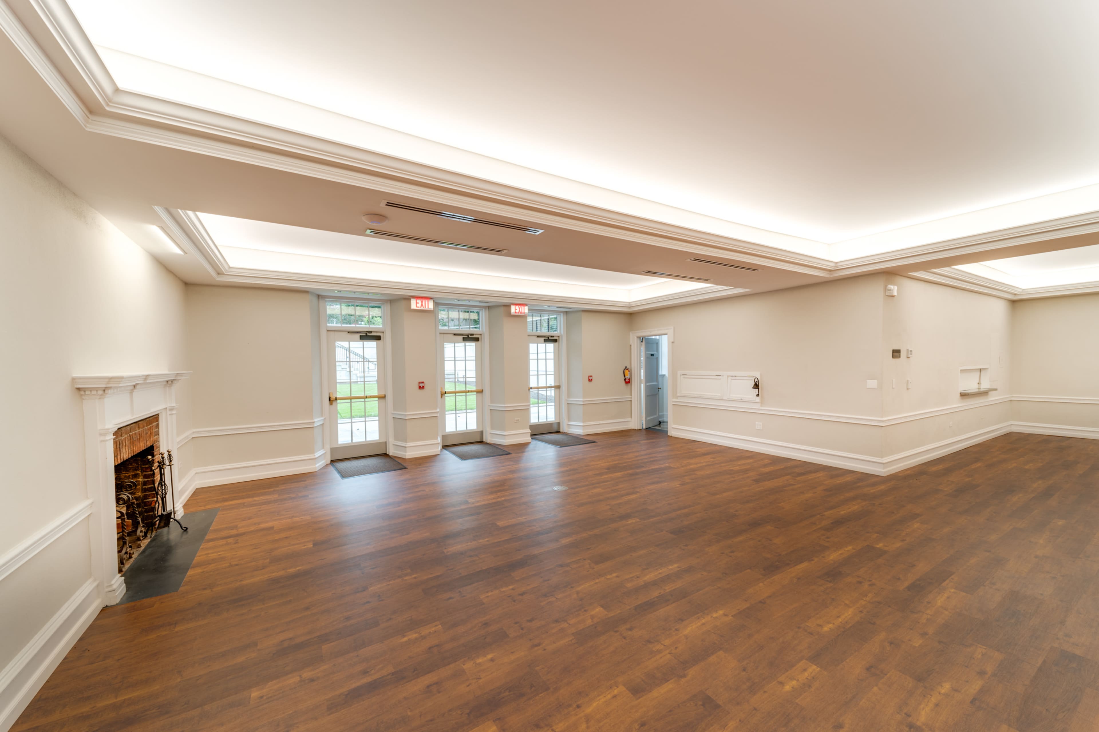 A spacious, empty room with hardwood flooring, large windows, and two sets of double doors leading outside.