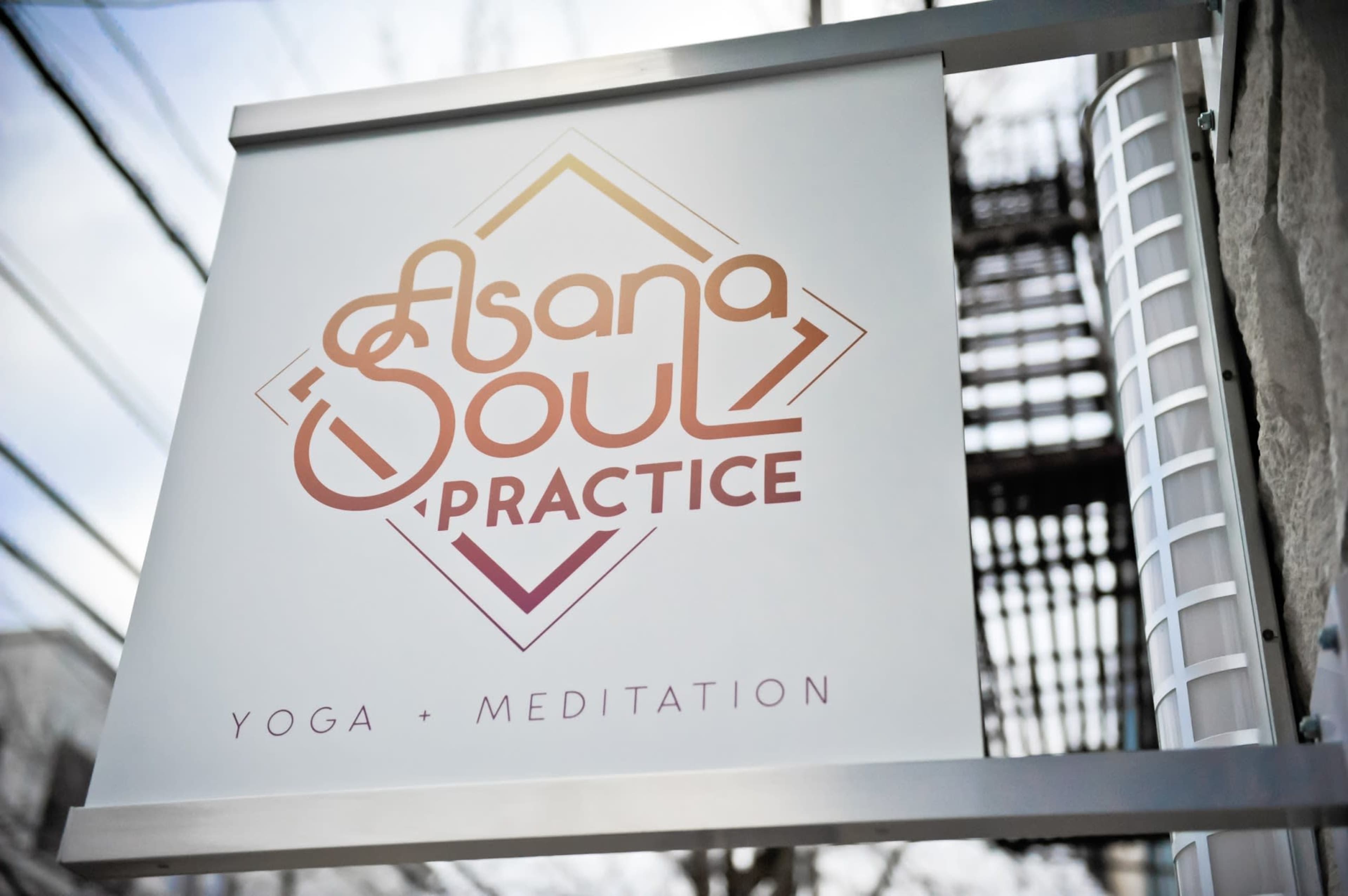 A sign for "Asana Soul Practice," advertising yoga and meditation services, hangs outside a building.