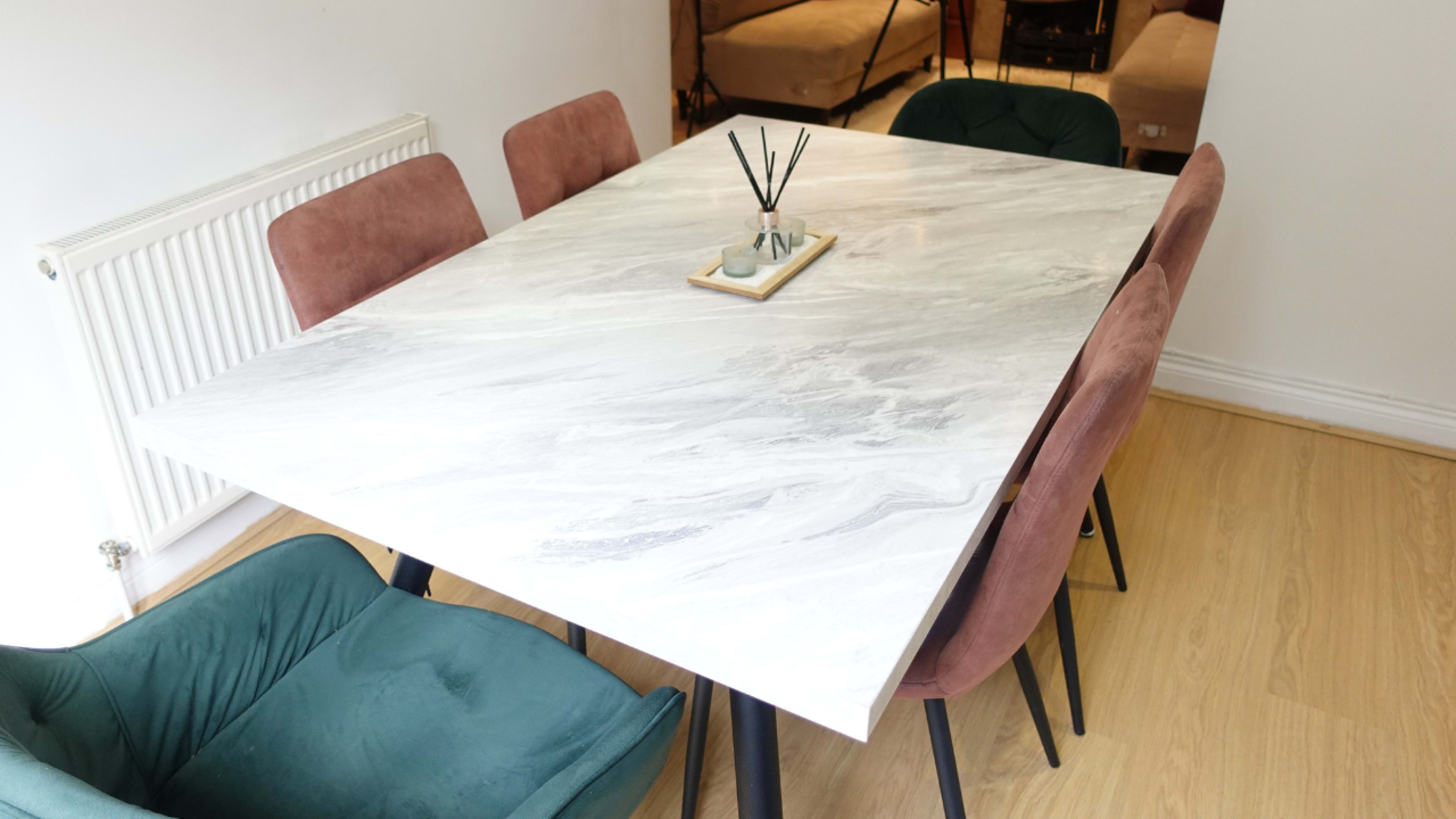 A marble dining table is set in a room with six chairs, featuring two green and four pink upholstered seats.