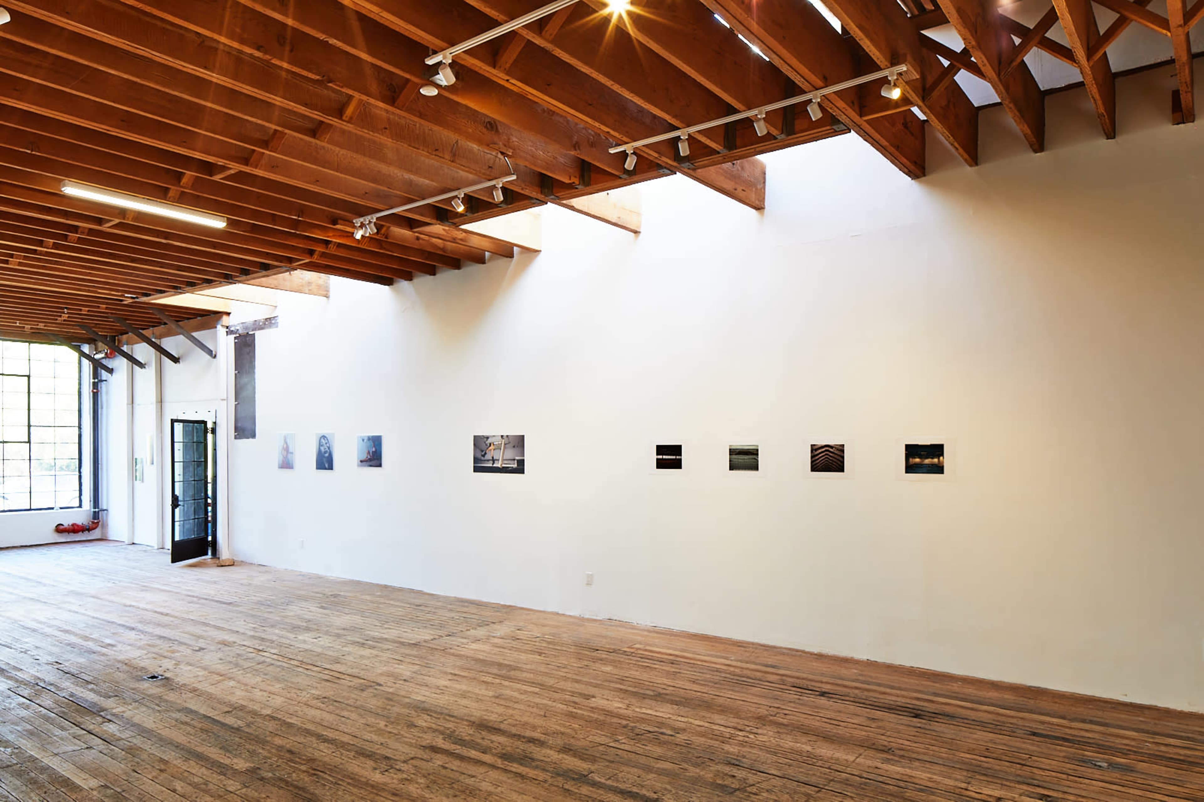 An empty art gallery with wooden floors and a row of framed photographs mounted on the white wall.