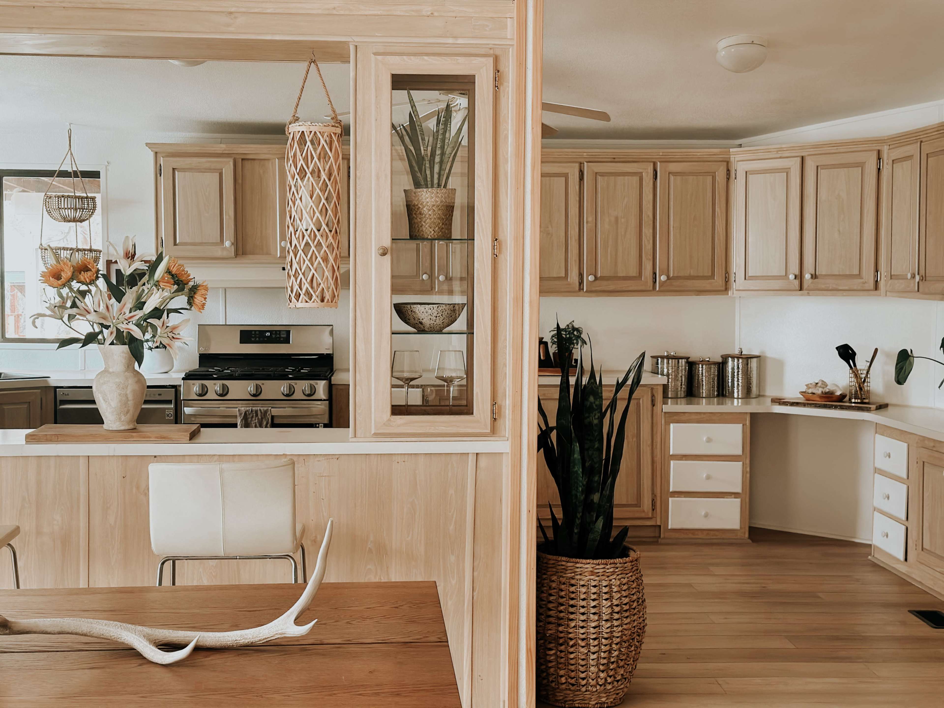 A modern kitchen with light wooden cabinets, a dining area featuring a wooden table, and decorative plants in various containers.