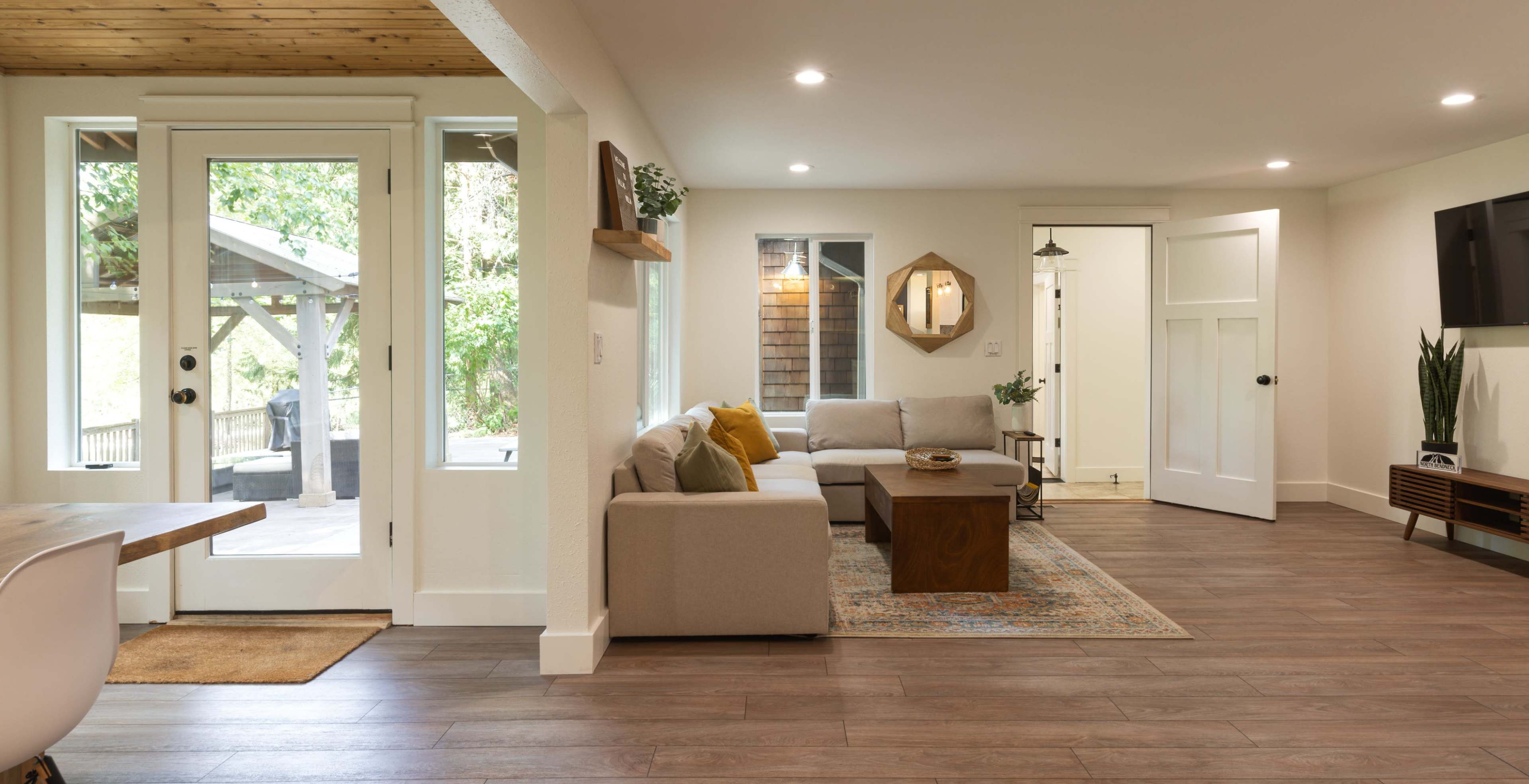 A modern living room with a light-colored sofa, a wooden coffee table, and large windows letting in natural light.