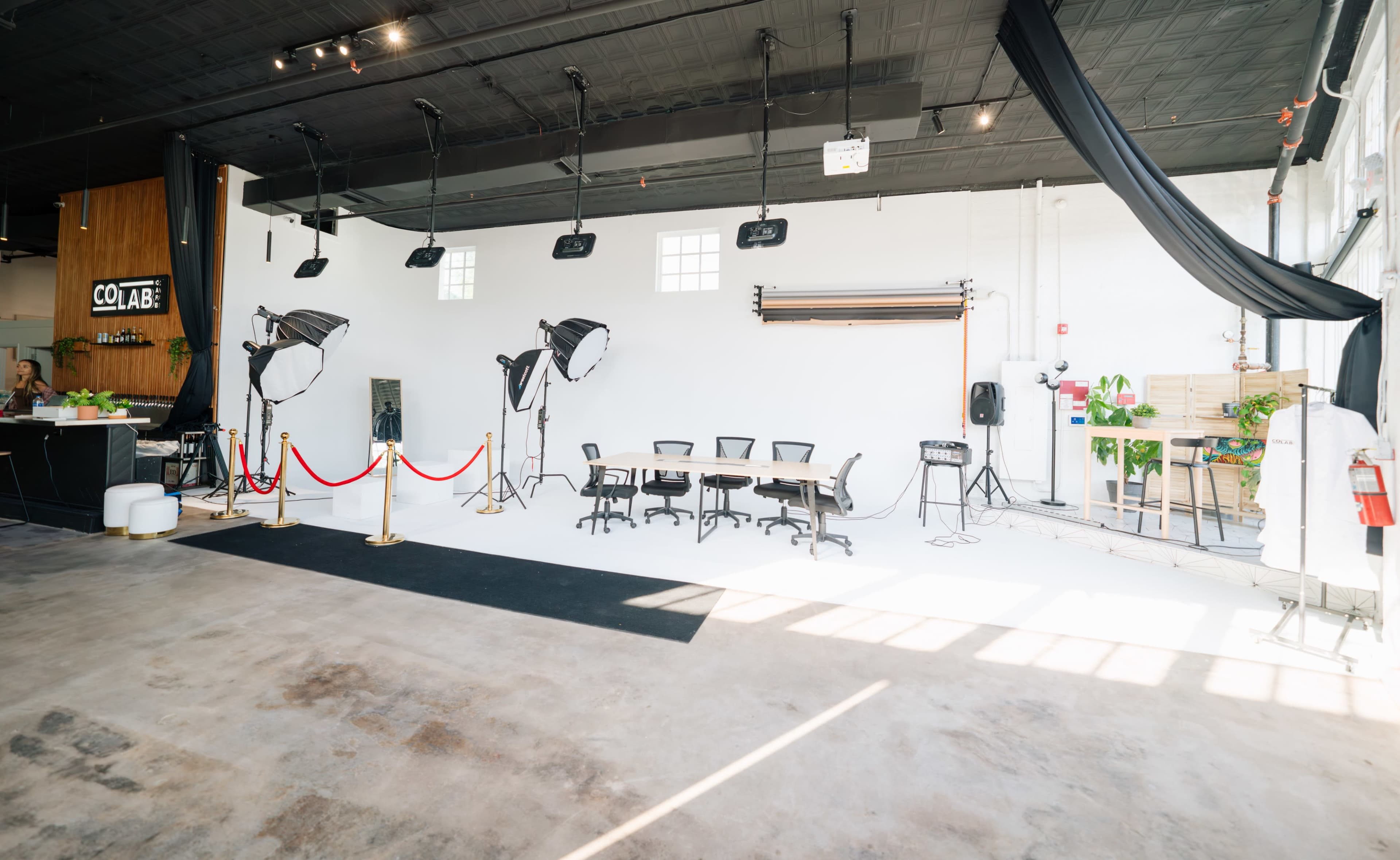 A spacious studio with a large white backdrop, several lights, and a round table surrounded by office chairs.