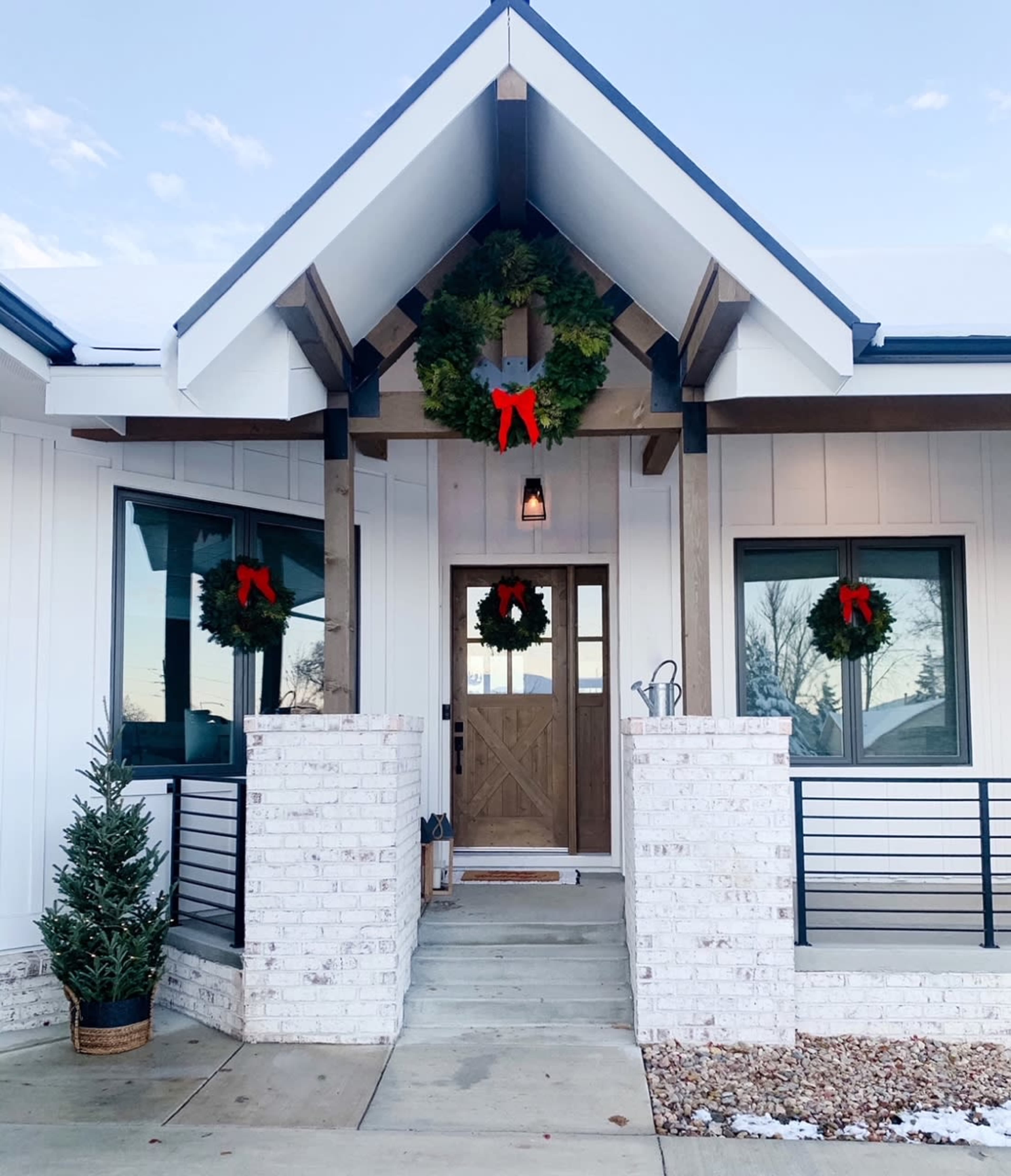 A modern home features a decorated entrance with holiday wreaths and a small pine tree on the porch.
