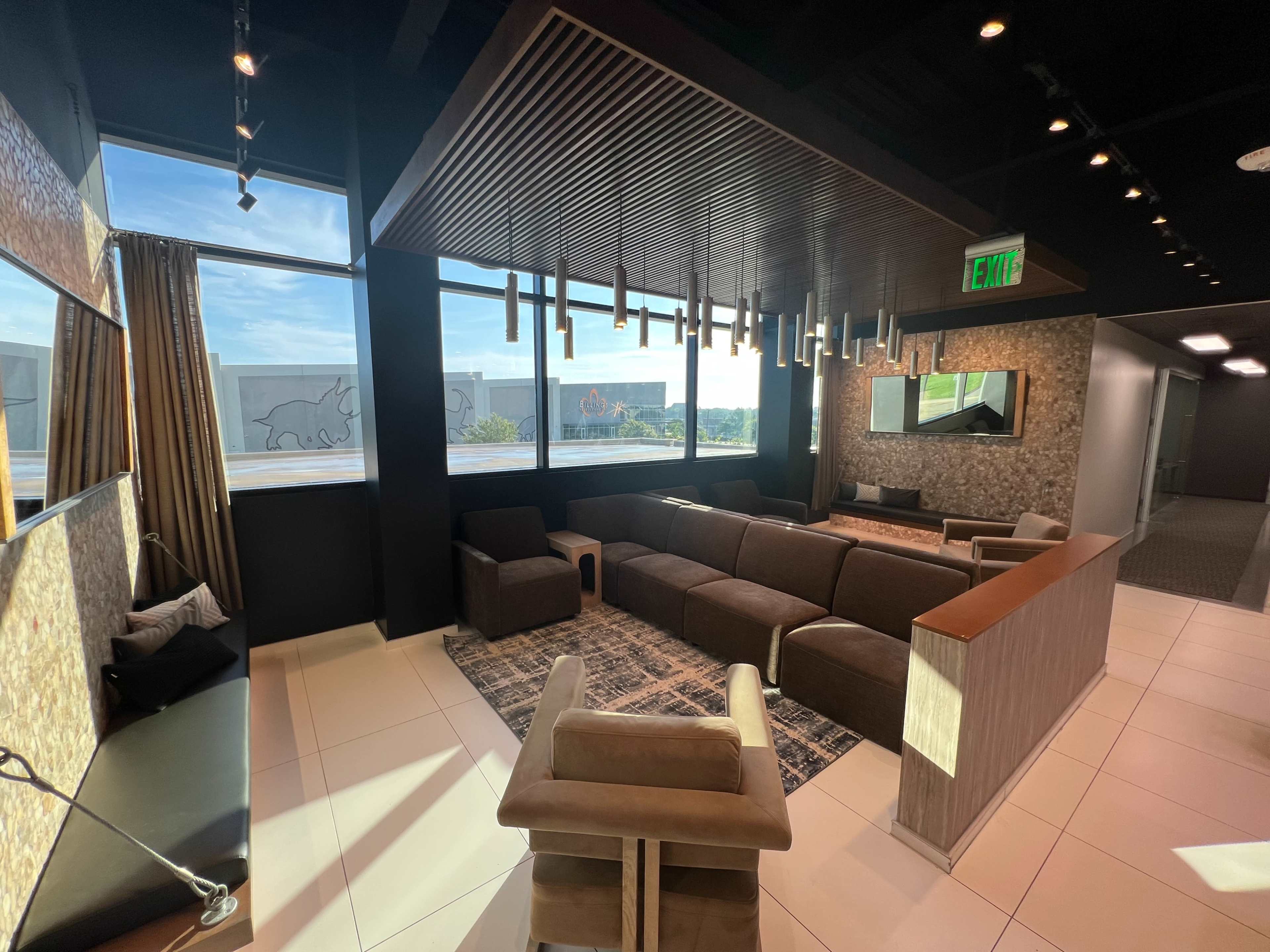 The image shows a modern lounge area with a mix of seating options, large windows, and decorative lighting.