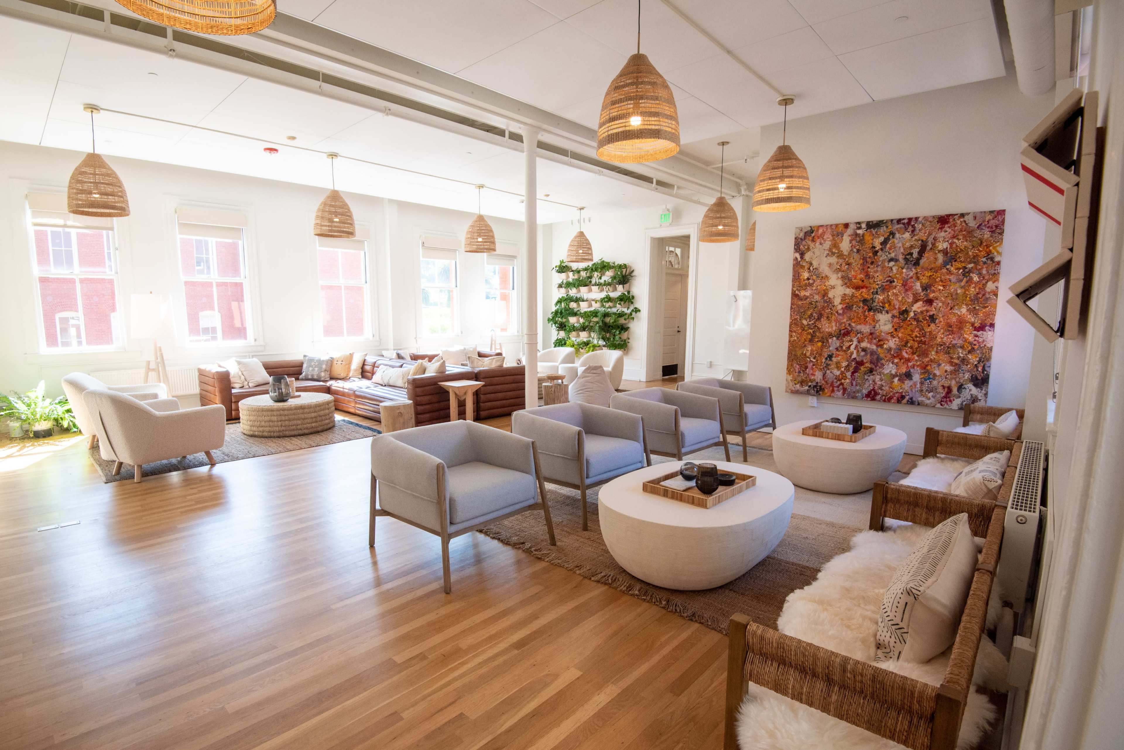 The image shows a spacious, modern lounge area with comfortable seating, large windows, and decorative pendant lights.