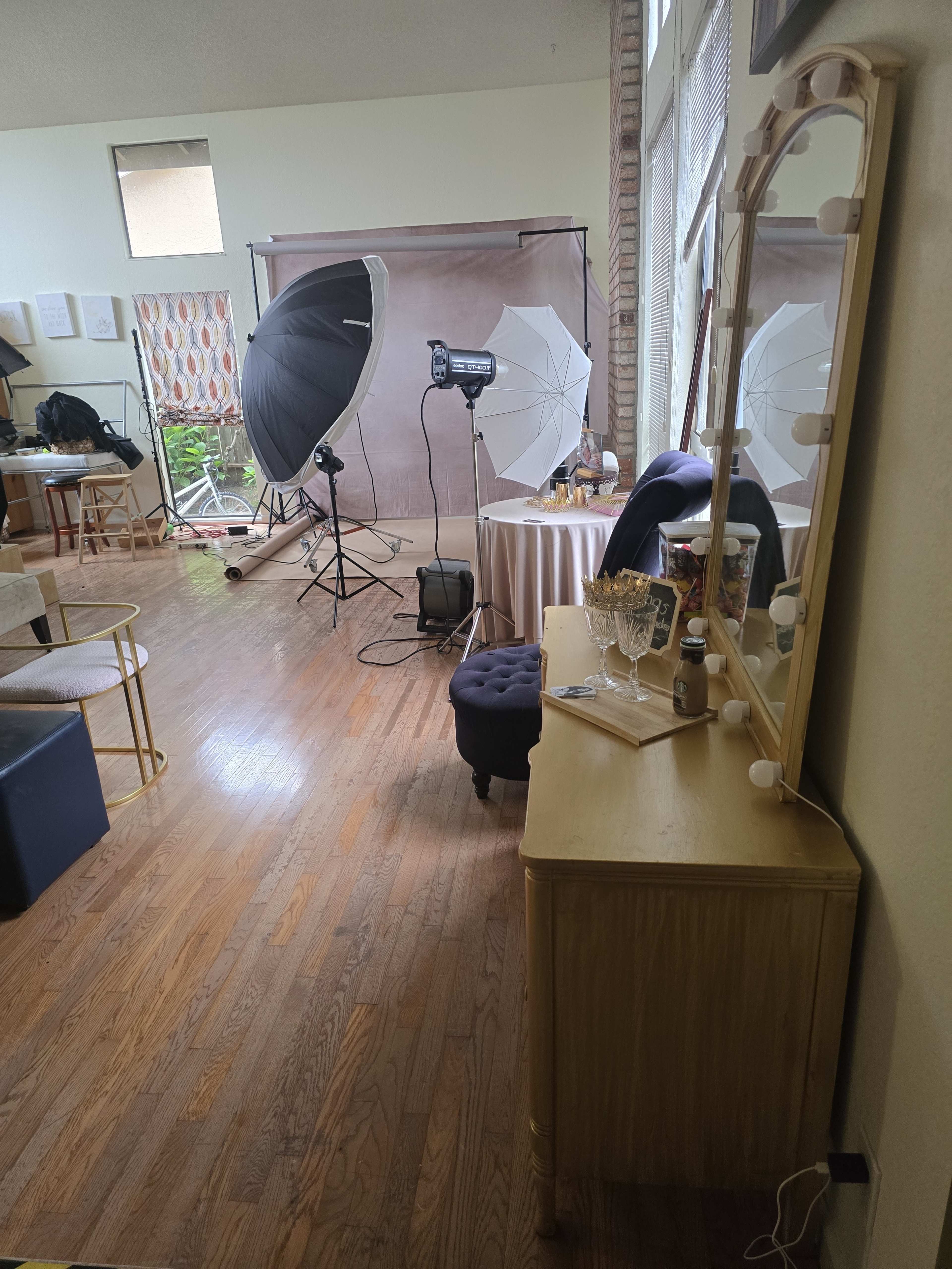 The image shows a photography studio setup with lighting equipment, a backdrop, and furniture in a spacious room.