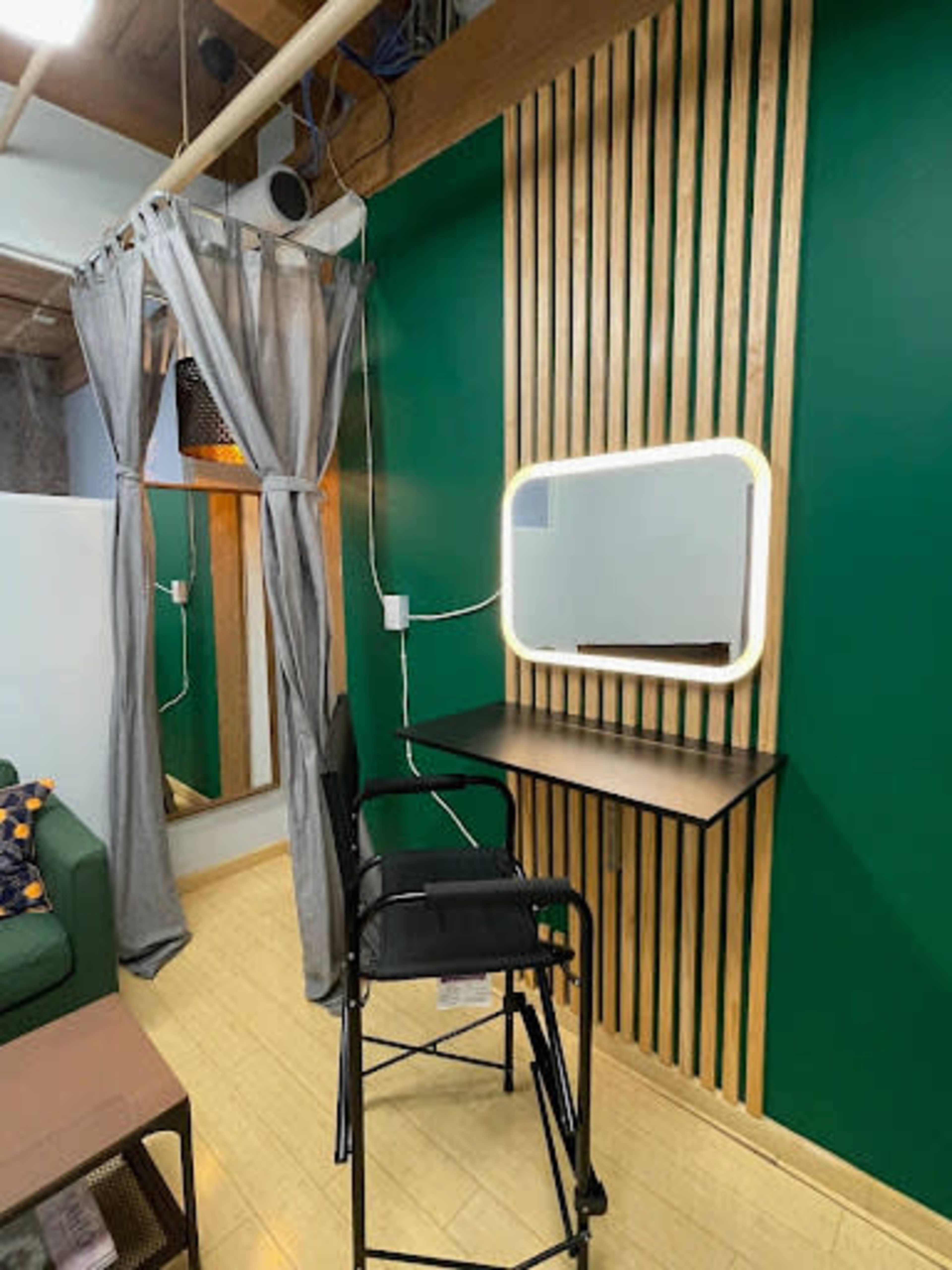 A modern vanity area with a mirror, a wooden wall with vertical slats, a black chair, and gray curtains in a green room.
