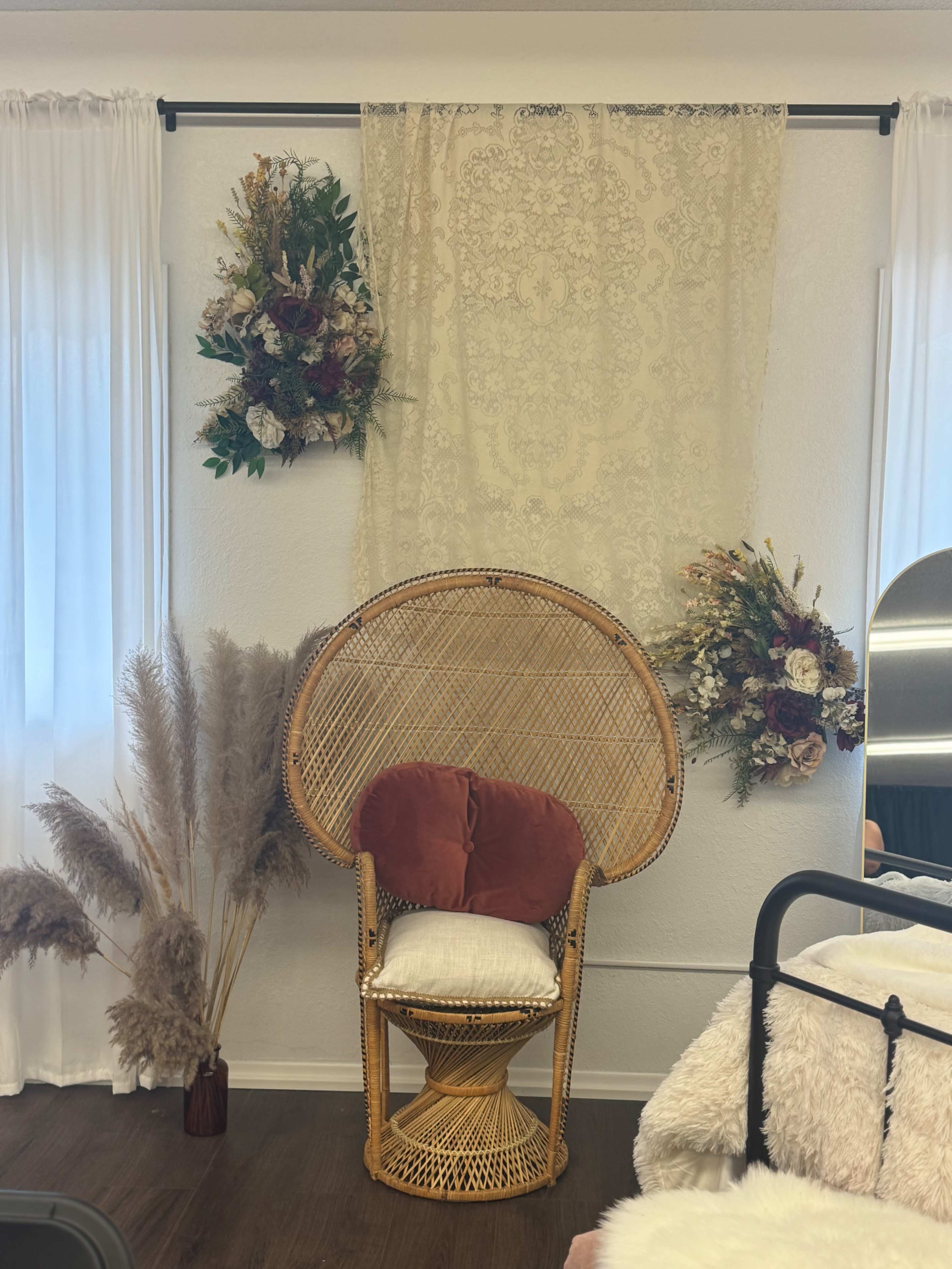 The image features a rattan chair with a cushion, positioned against a wall adorned with a lace fabric and floral arrangements.