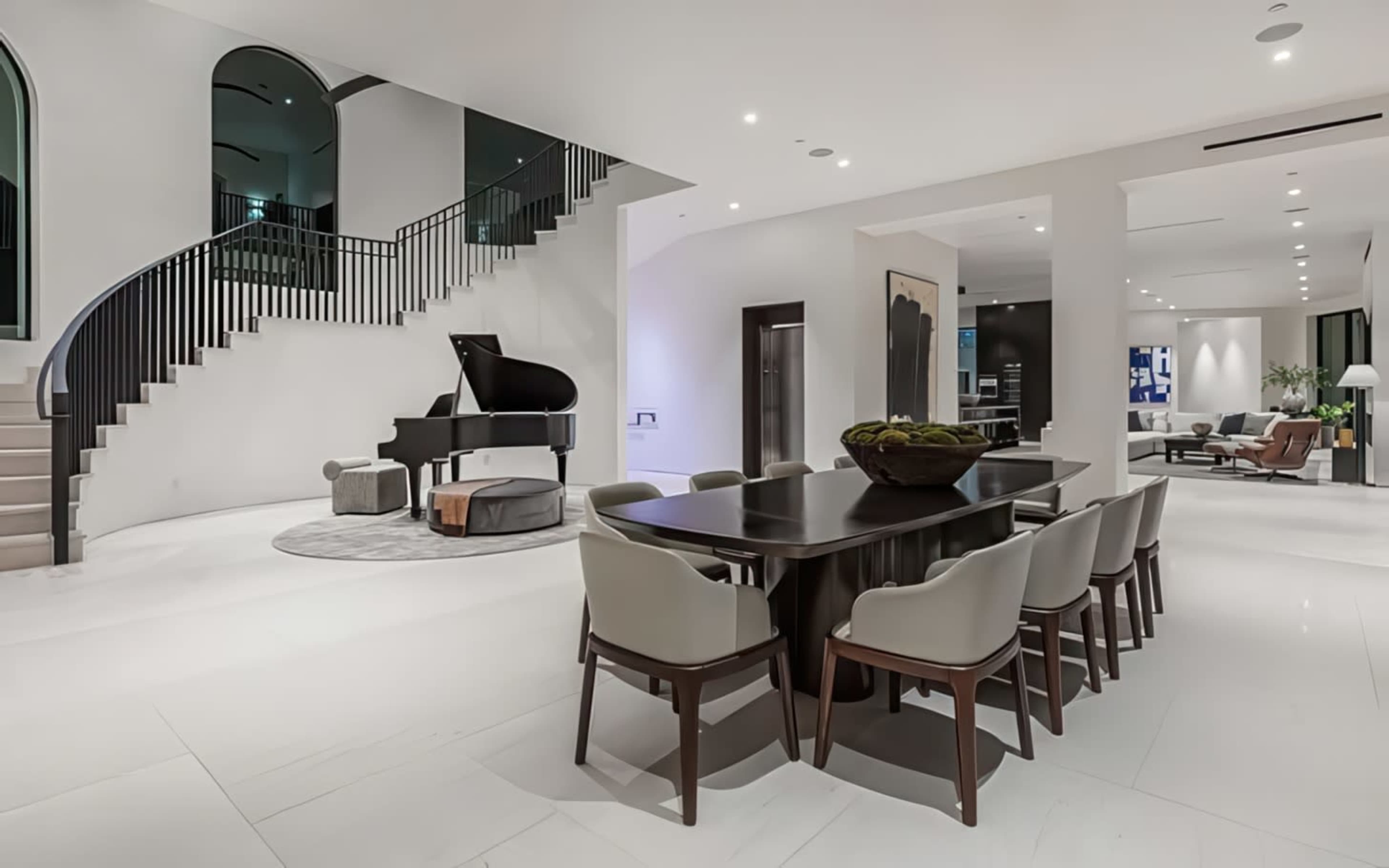 The image shows a spacious, modern interior featuring a dining area, a grand piano, and a staircase with a contemporary design.