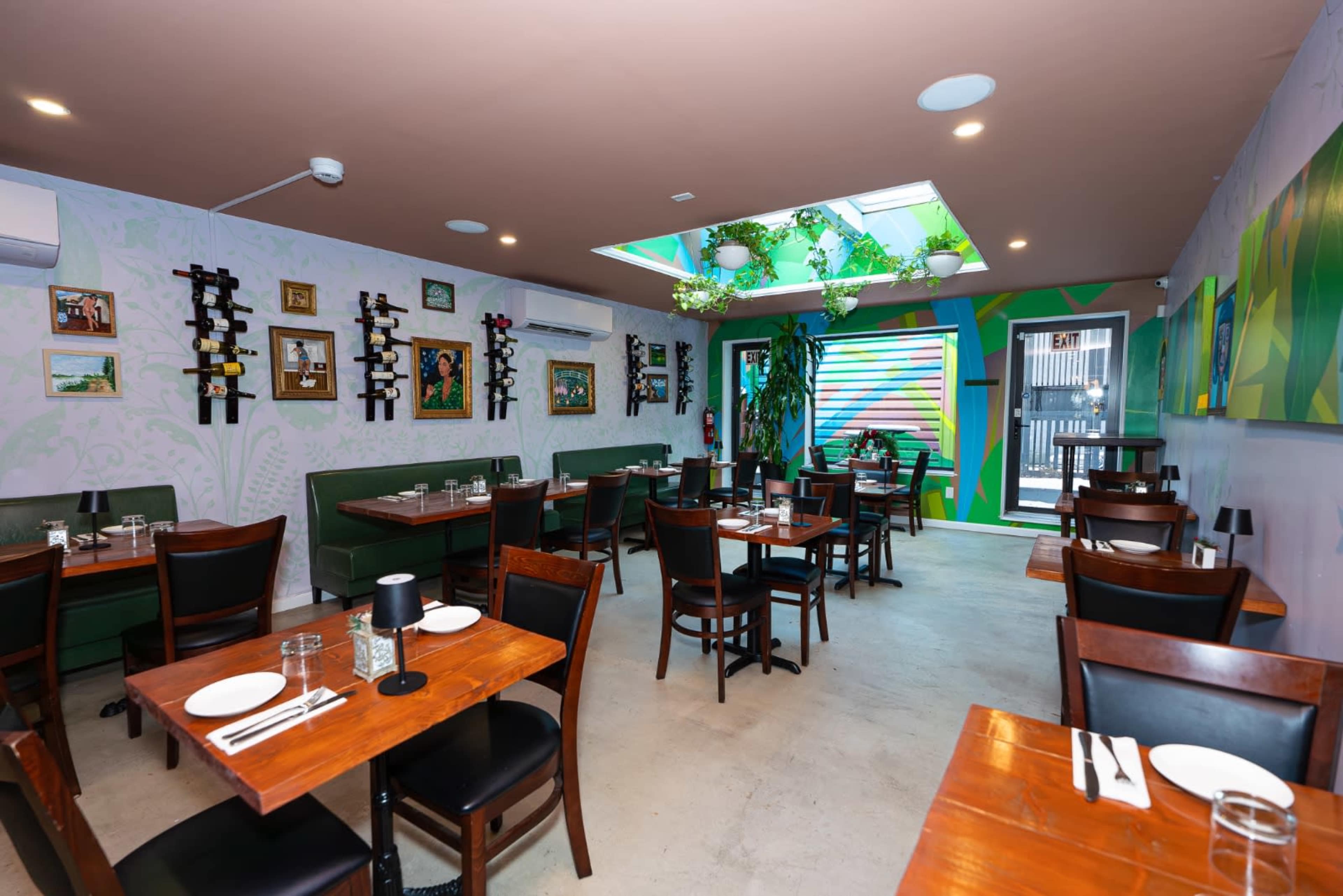 The image shows a restaurant interior with wooden tables, black chairs, and a skylight, featuring green and colorful wall art.