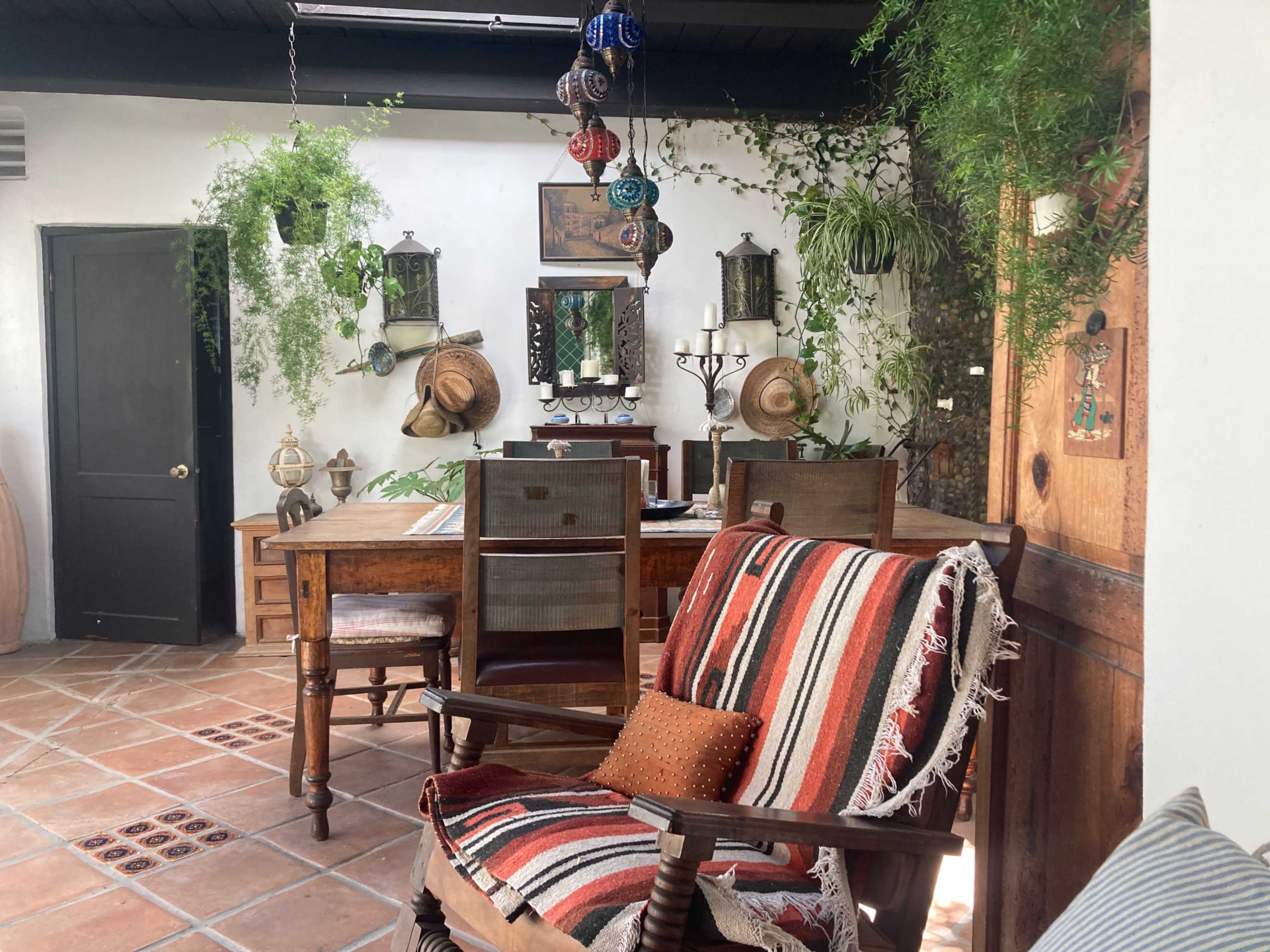 A rustic dining area featuring a wooden table surrounded by chairs, adorned with plants and wall decorations.