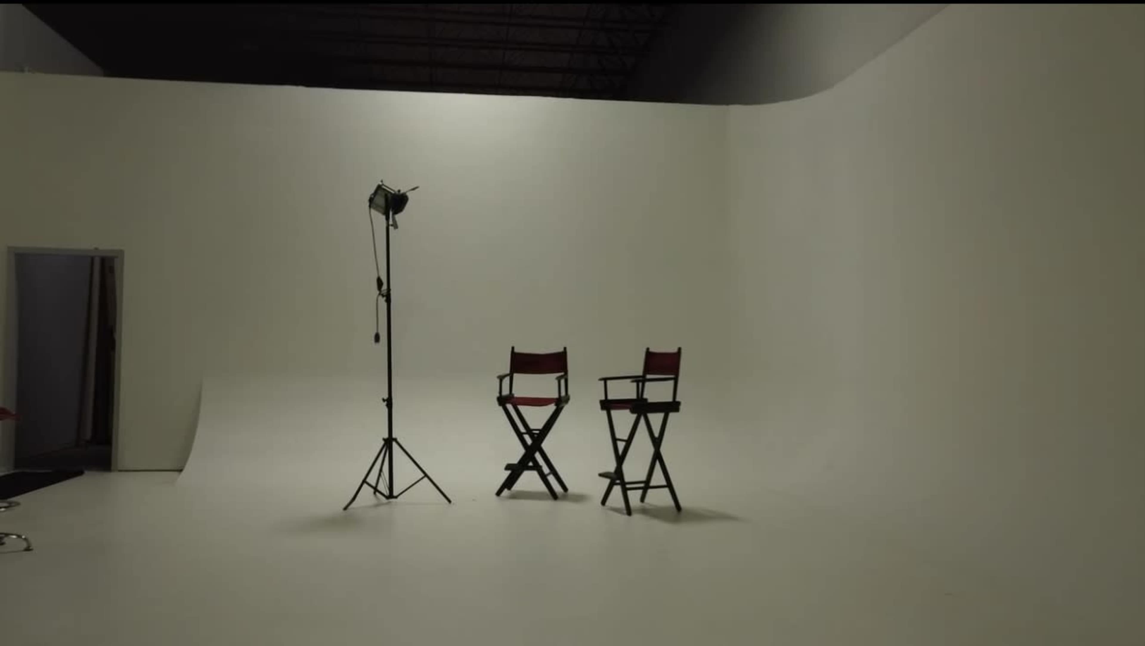 A photography studio features two red director's chairs beside a standing light on a plain white backdrop.