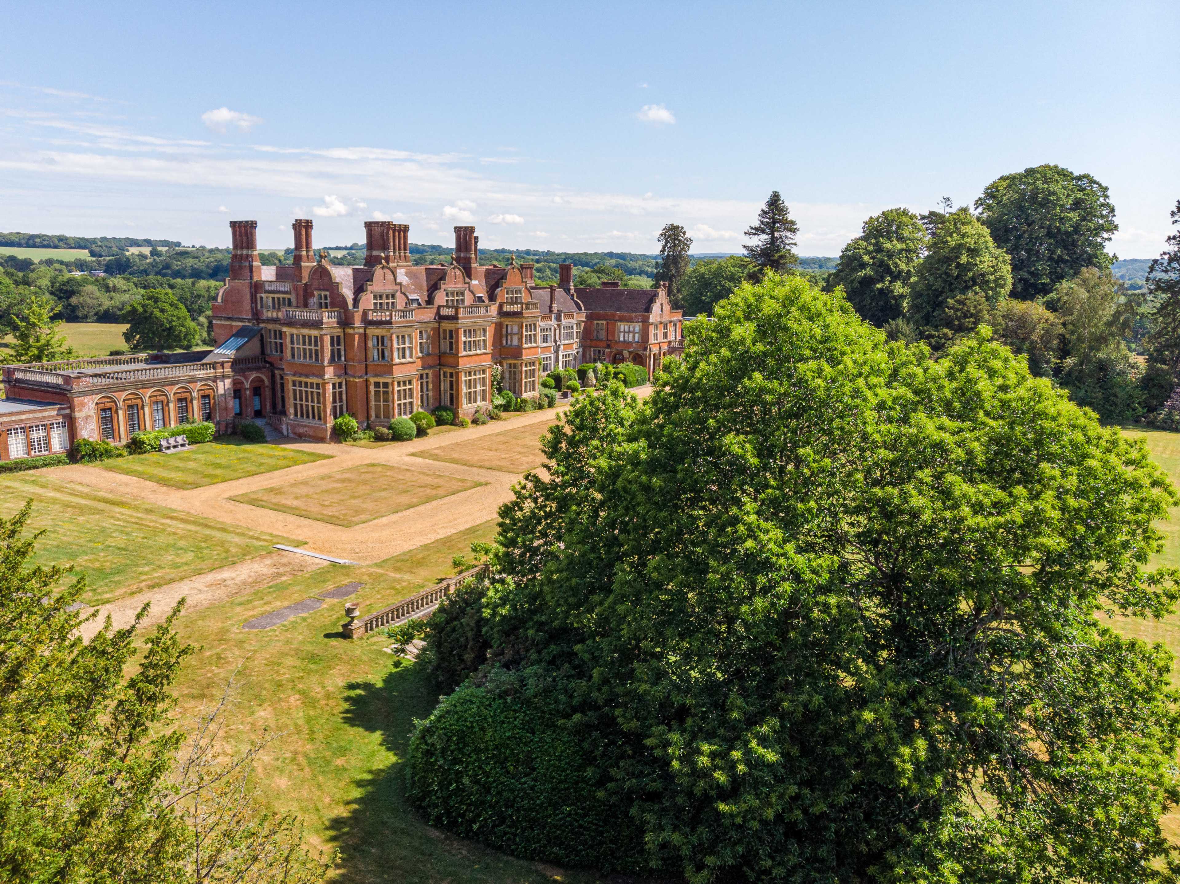 A large, ornate mansion surrounded by greenery and open fields under a clear blue sky.