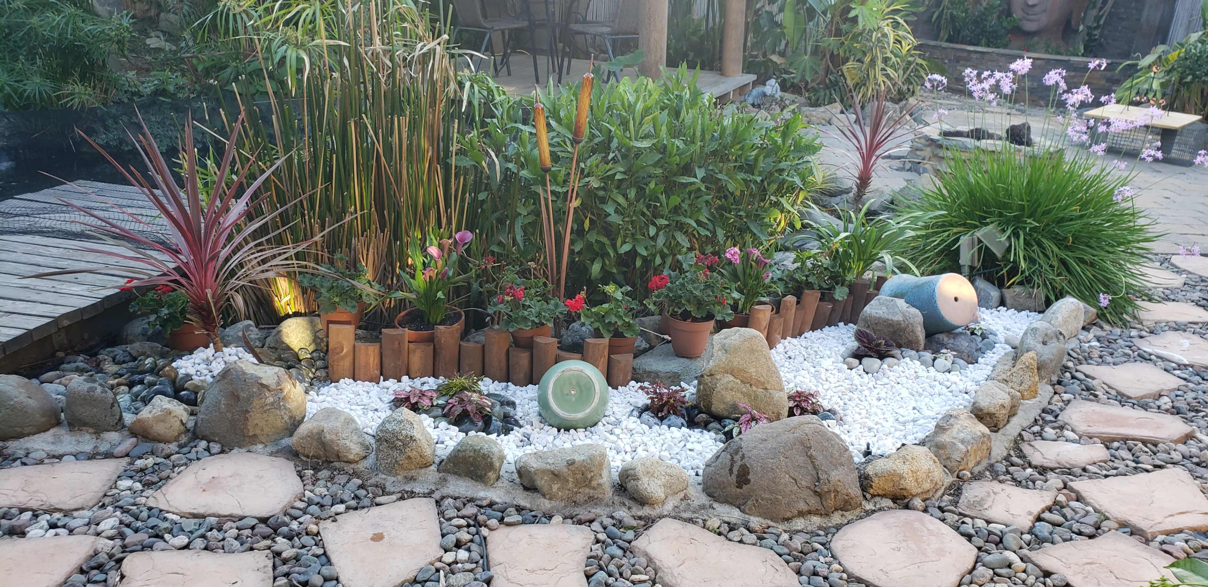 A landscaped garden featuring potted plants, decorative stones, and a pathway made of stone slabs.