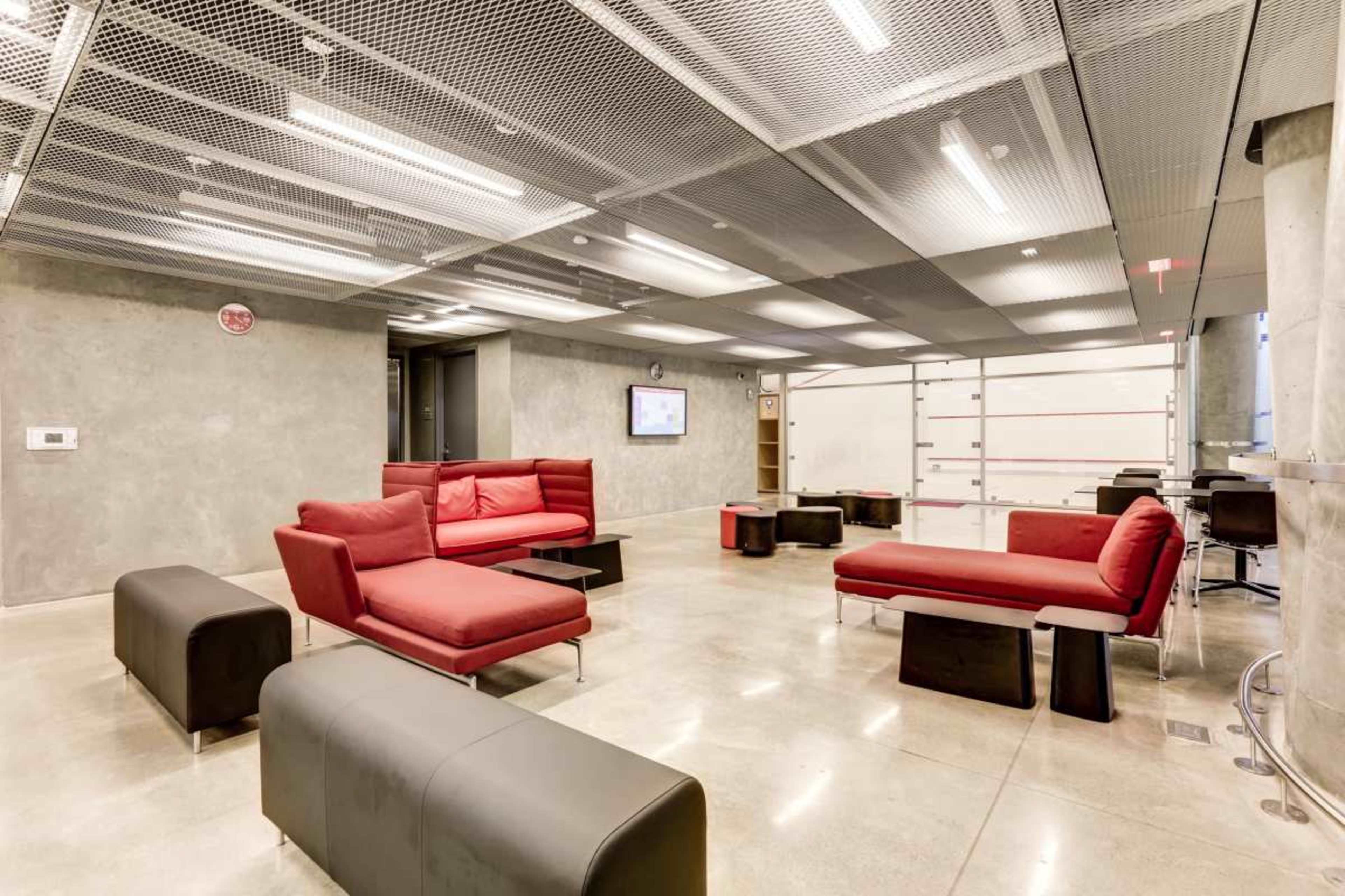 The image shows a modern lounge area with red seating arrangements and black benches on a polished concrete floor.