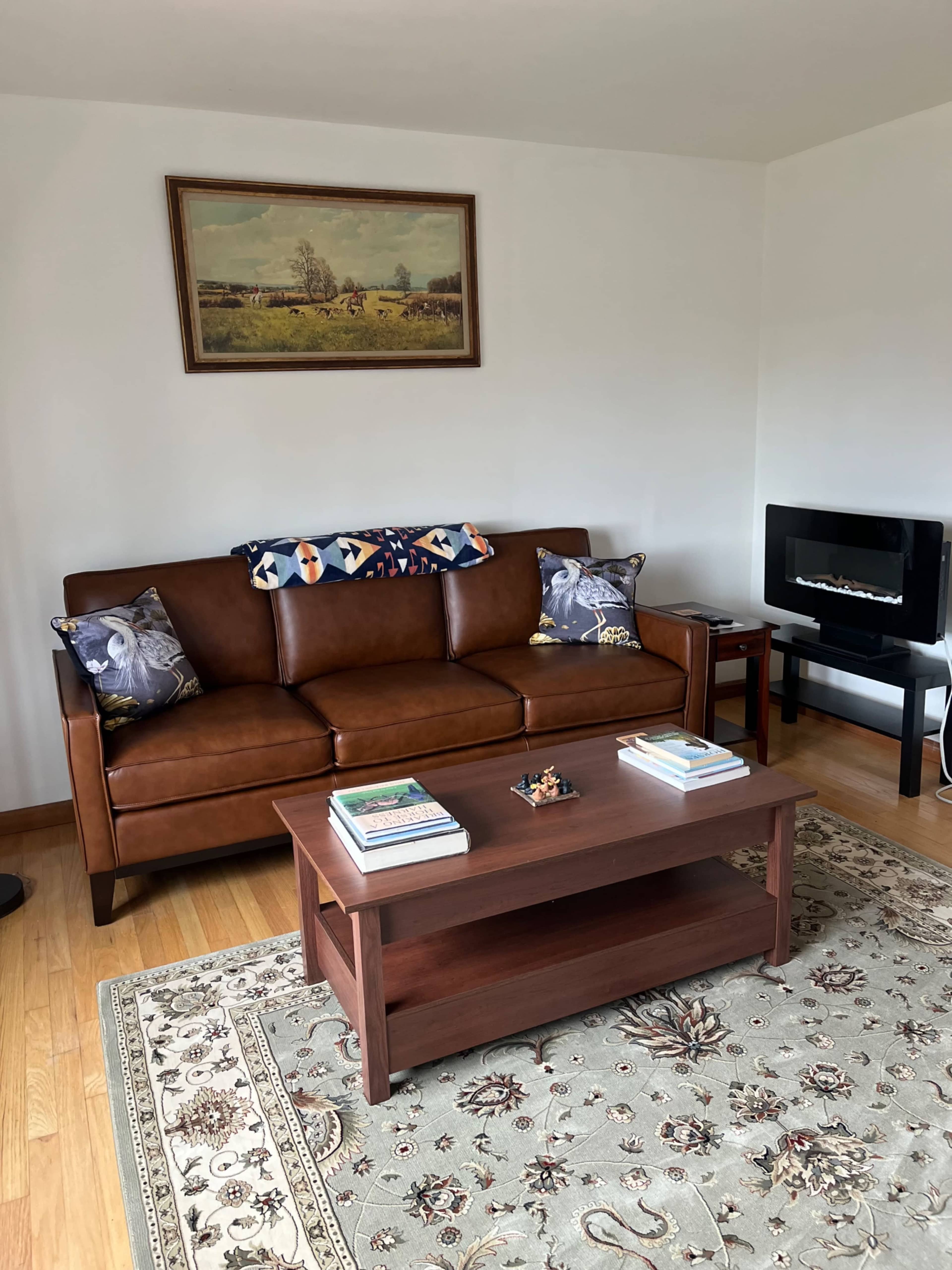 The scene shows a living room with a brown leather sofa, a wooden coffee table displaying books, and a decorative painting on the wall.
