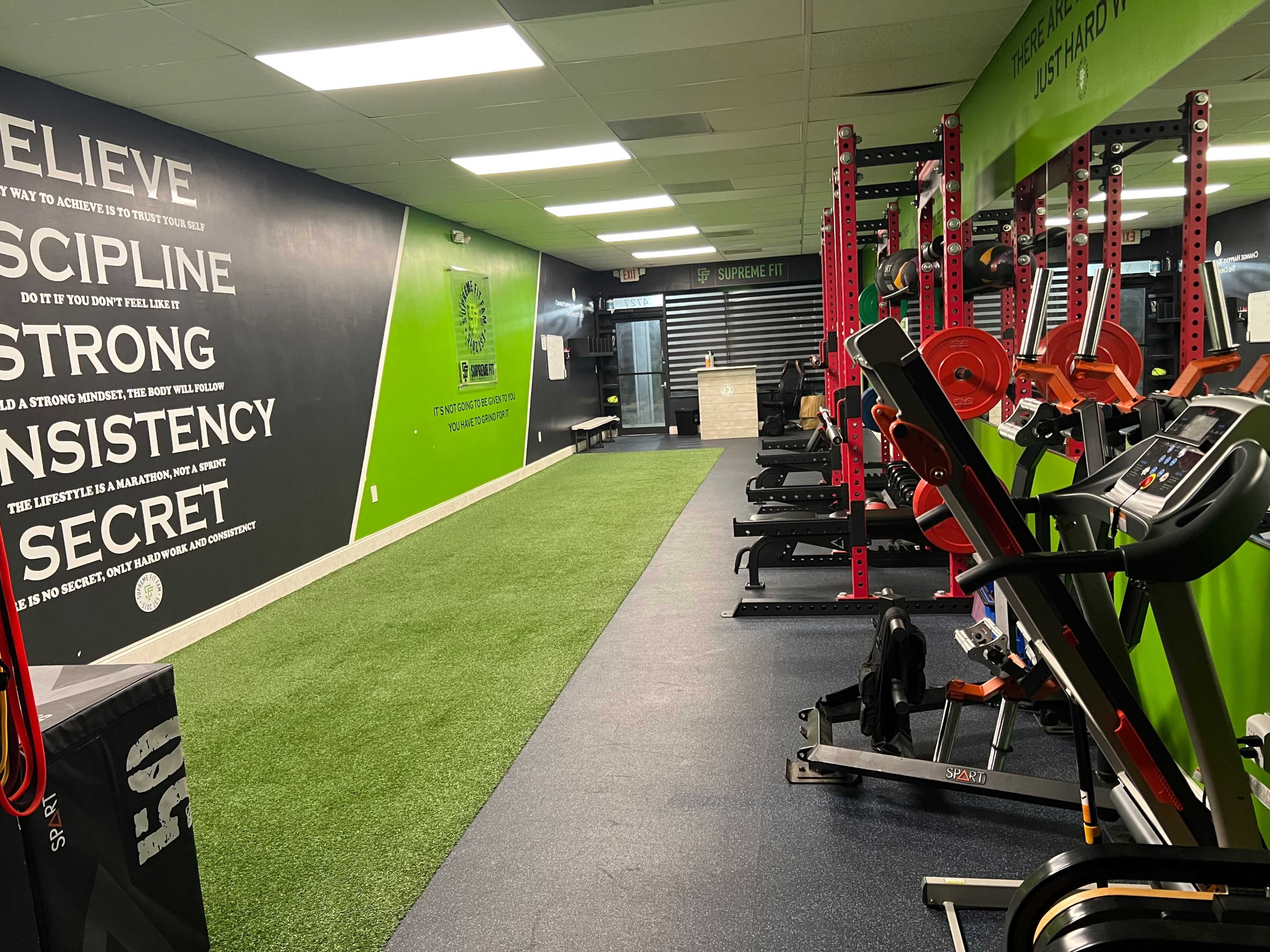 A gym interior with weightlifting equipment, cardio machines, and motivational wall graphics.