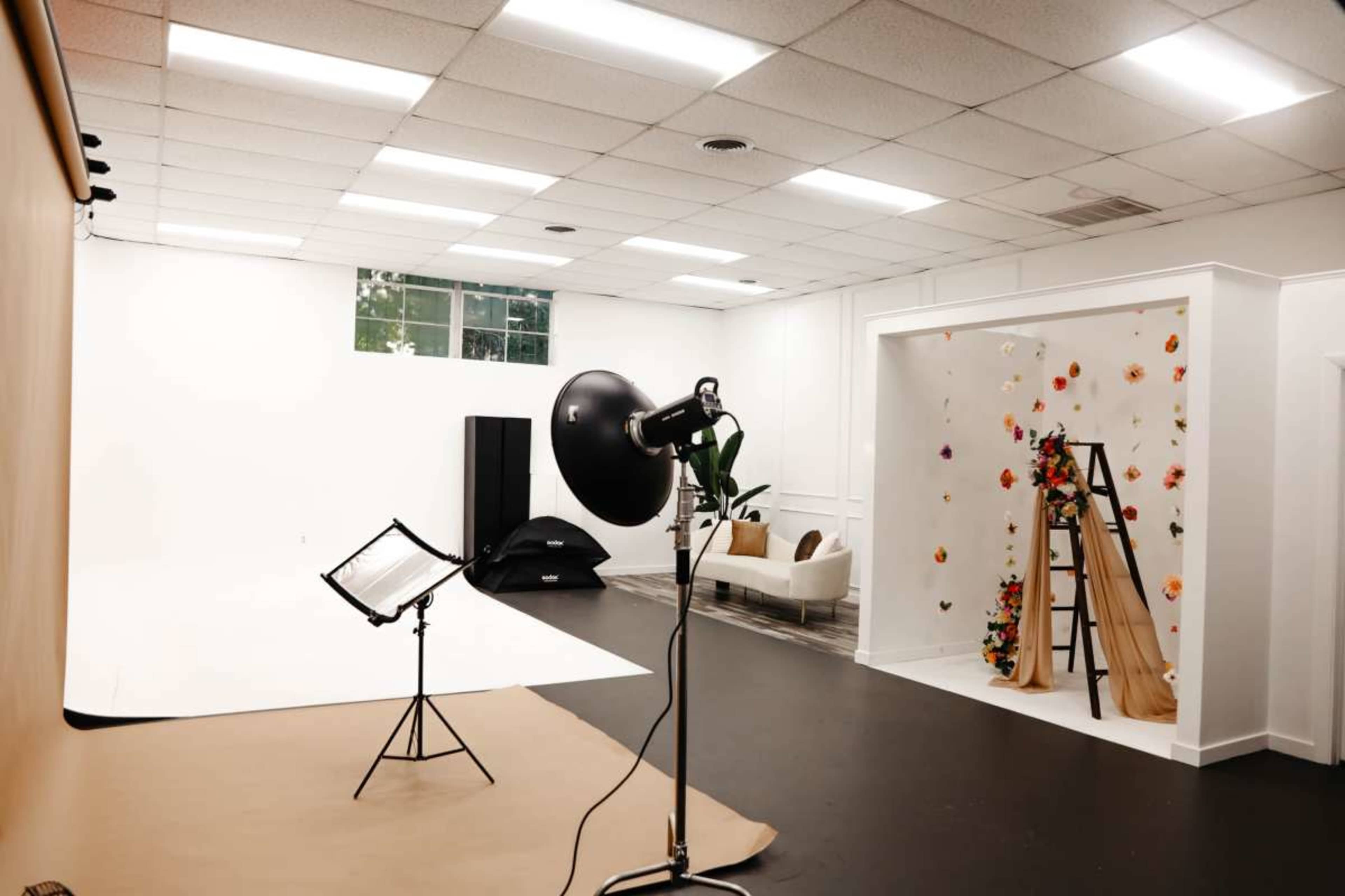 A photography studio with a backdrop, lighting equipment, and an area decorated with flowers and a ladder.