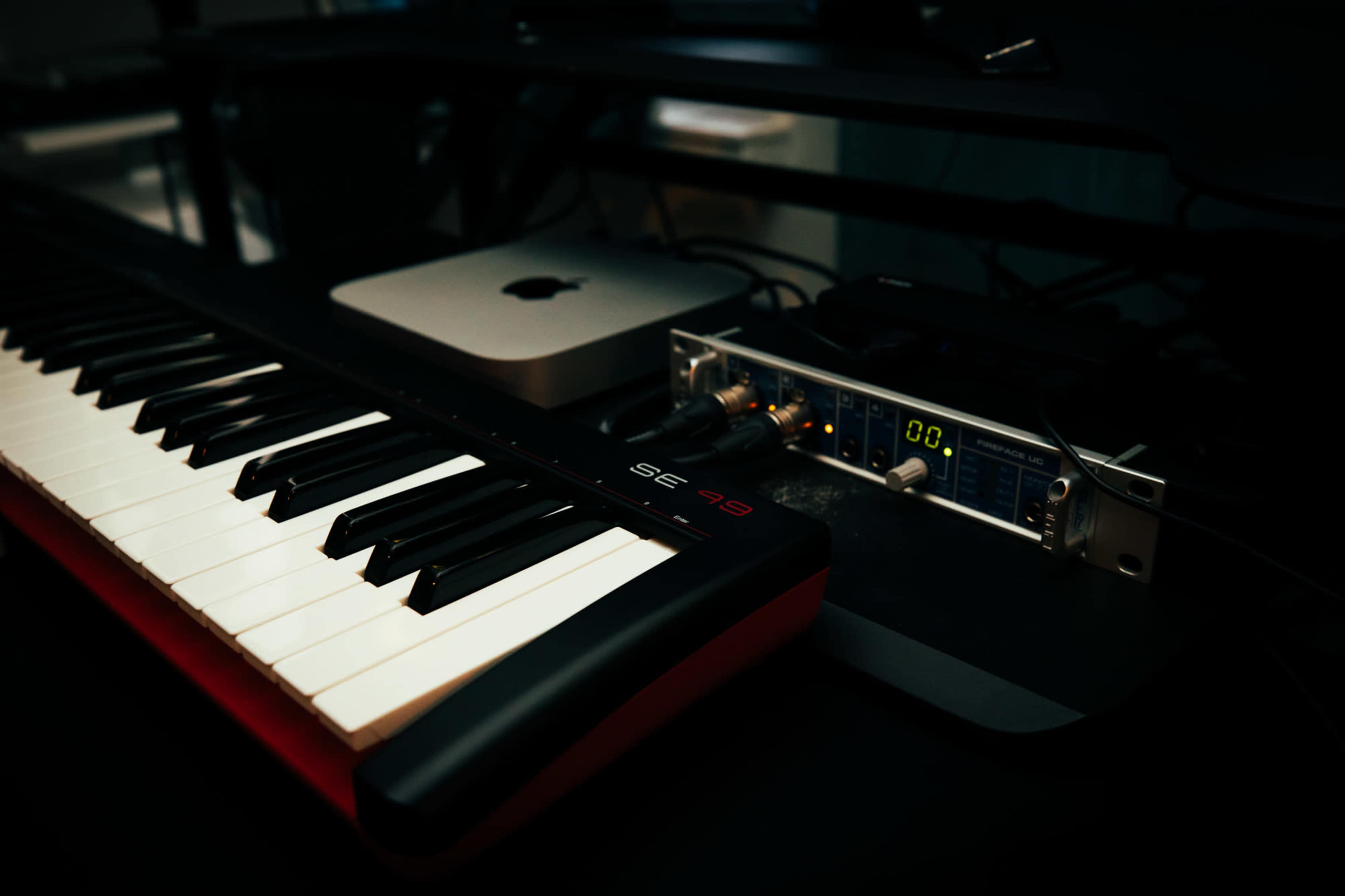 A black and white keyboard is positioned next to an audio interface connected to a computer.
