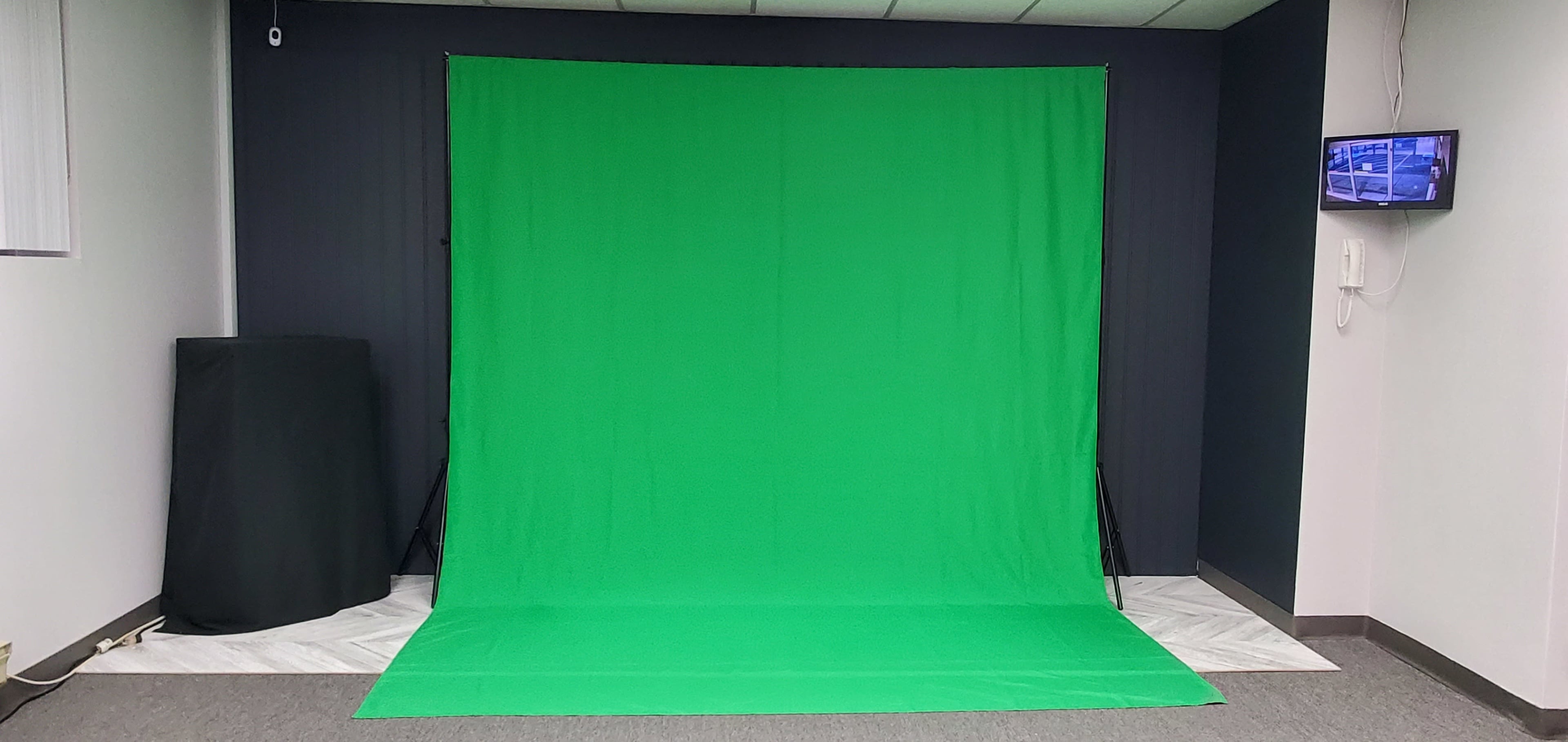 A green backdrop set up in a room, with a flat surface and a small screen mounted on the wall.