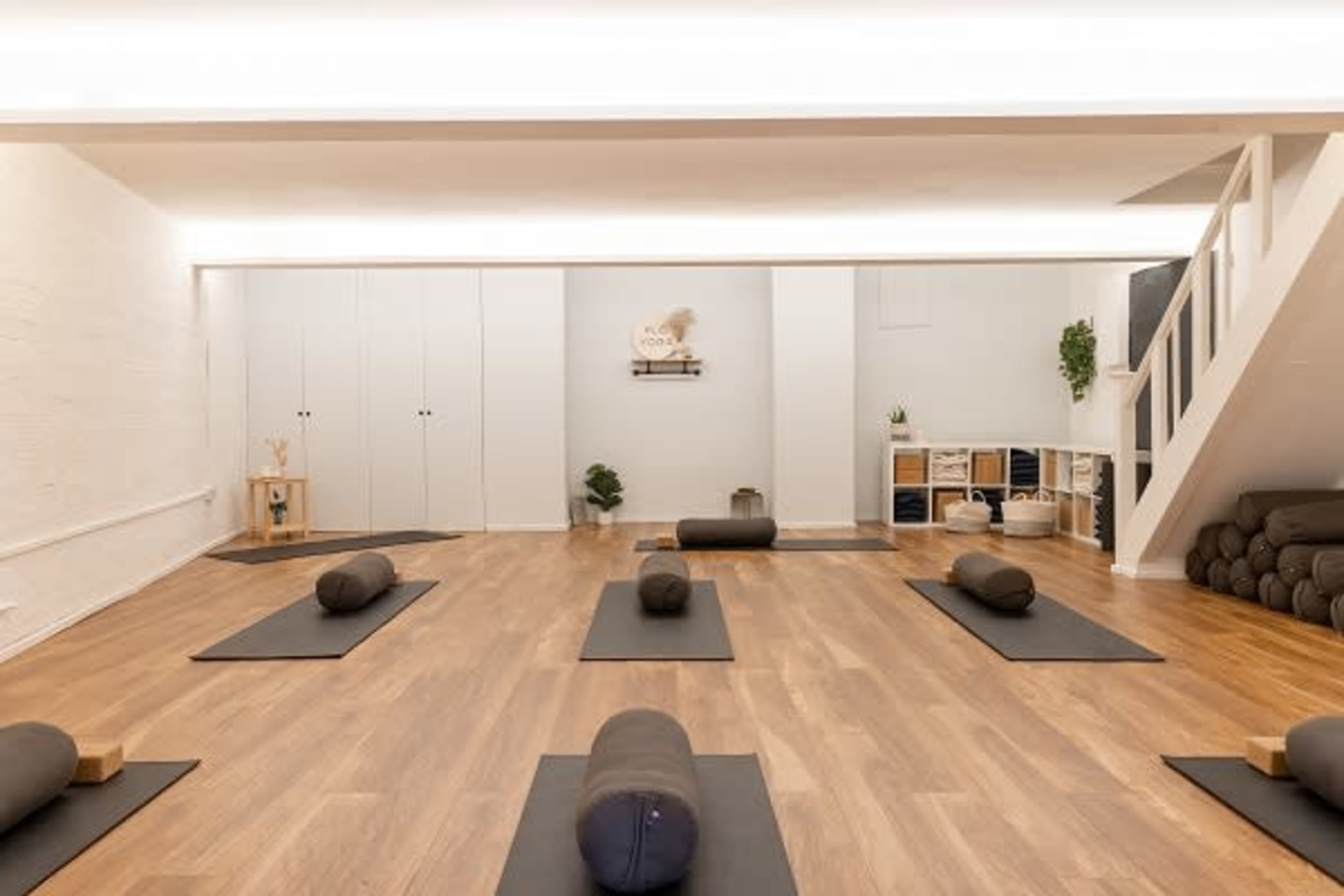 A yoga studio with several mats and props arranged neatly on a wooden floor, illuminated by soft overhead lighting.