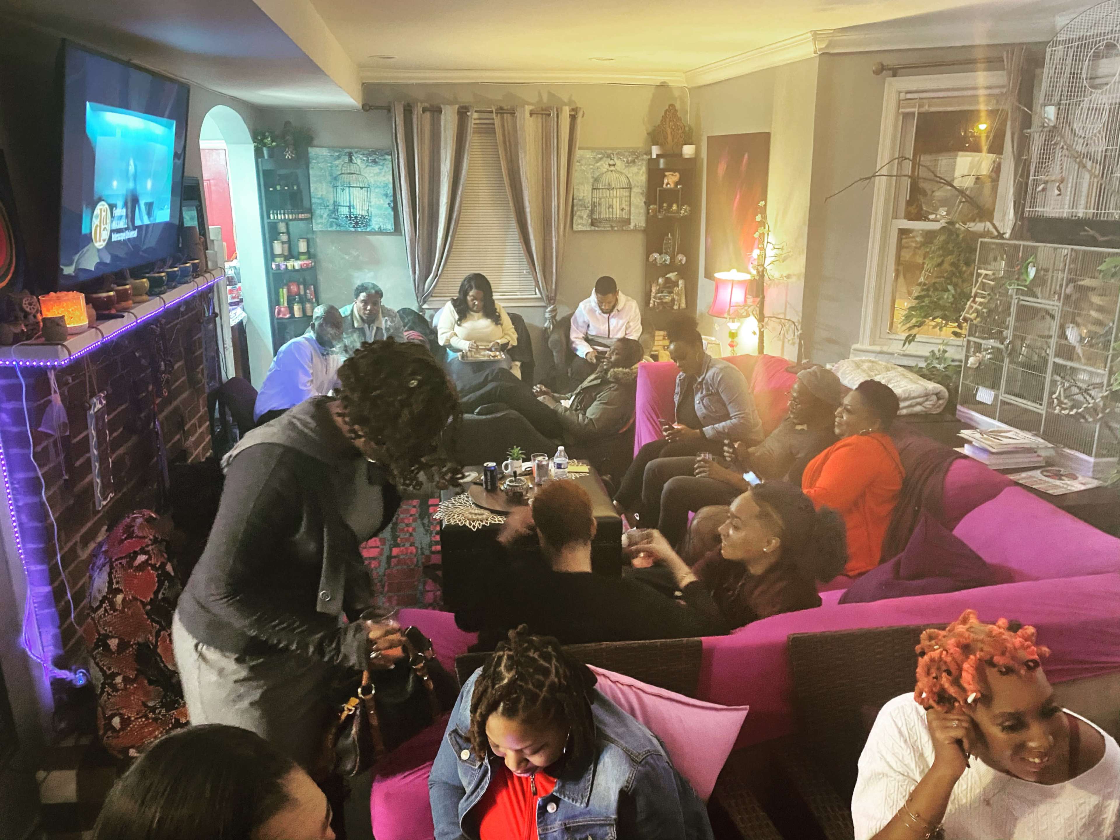 A gathering of people socializing in a cozy living room with colorful sofas and a television displaying a show.