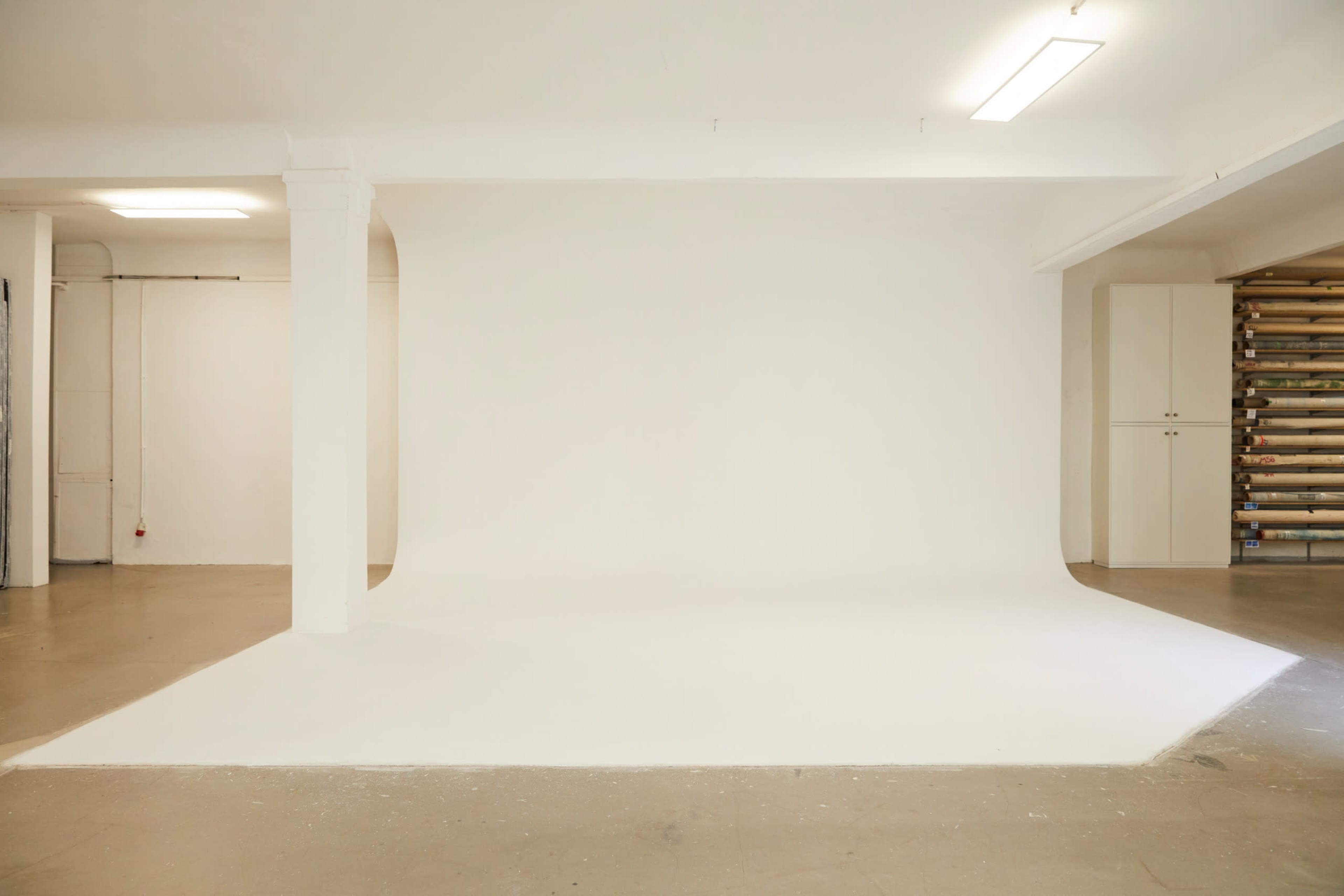 A spacious, empty studio featuring a white backdrop and smooth concrete flooring.