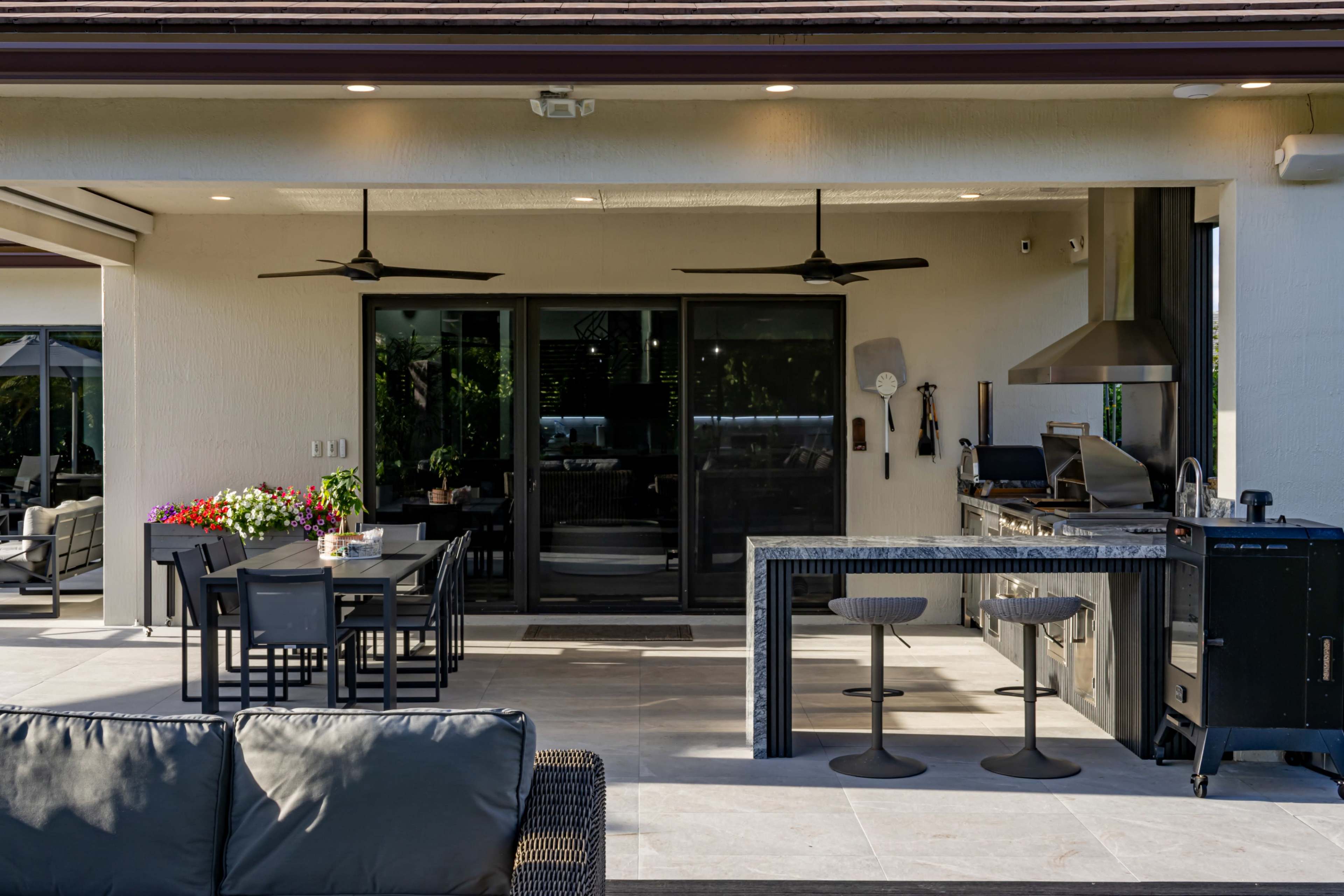 A modern outdoor patio features a dining table, a kitchen area with a grill, and comfortable seating.