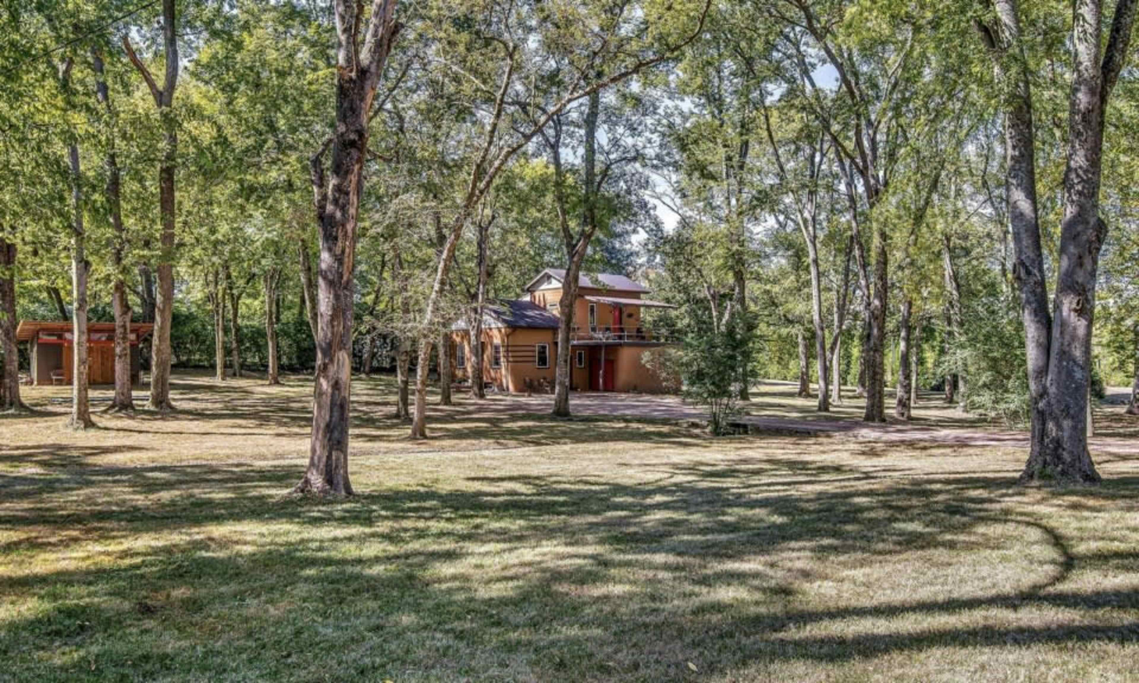 A two-story house is set among tall trees in a grassy area.