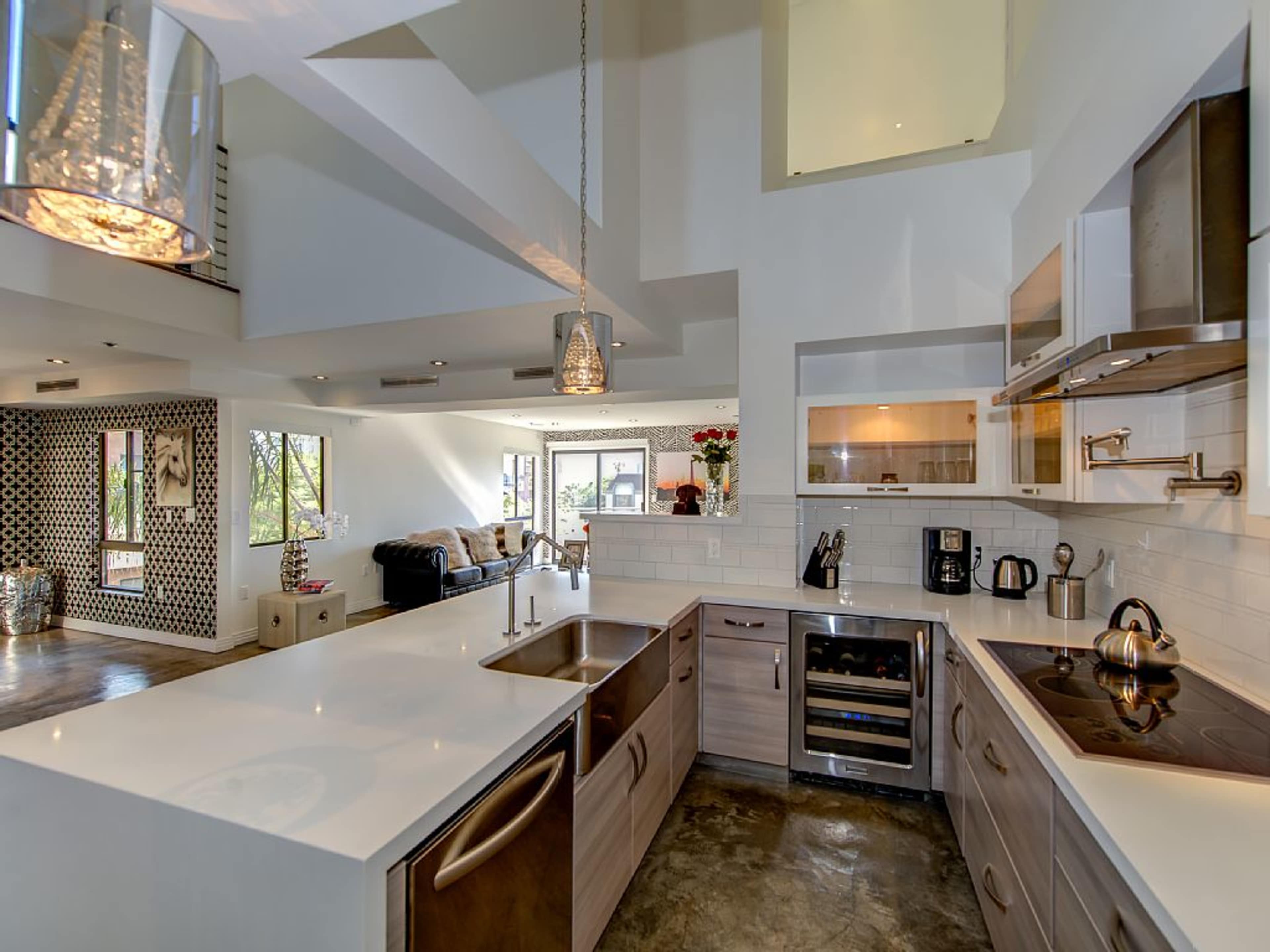 A modern kitchen with a central island featuring dual sinks and sleek cabinetry, opening up to a living area with large windows.